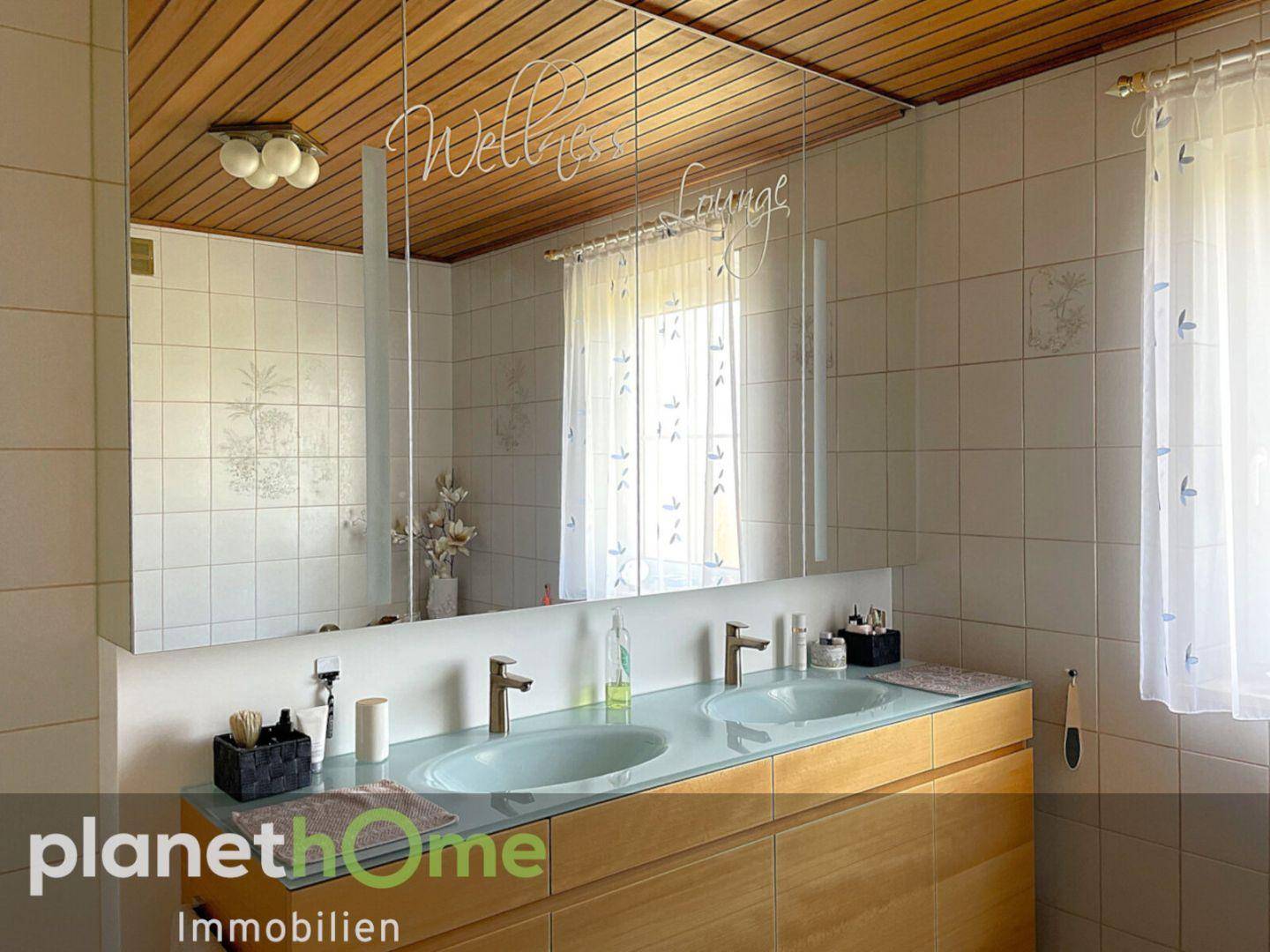 Badezimmer mit Doppelwaschbecken, großem Spiegelschrank und Holzdeckenverkleidung.