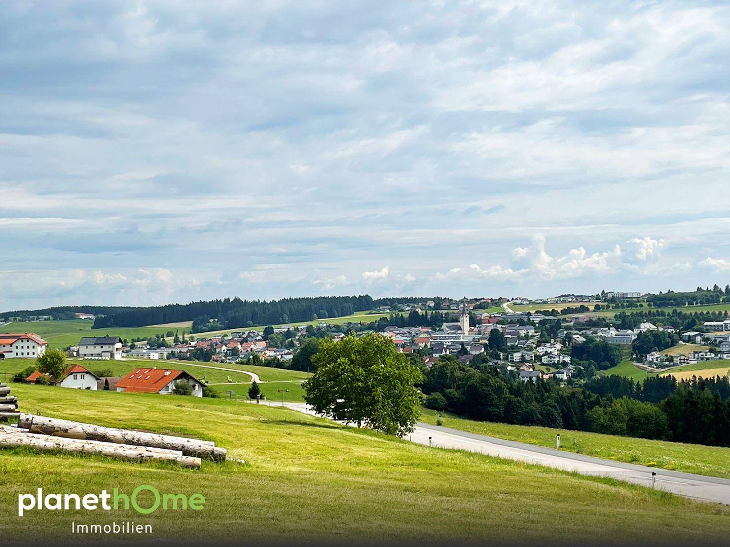 Panoramablick auf eine ländliche Ortschaft mit weiten Feldern und Wäldern.