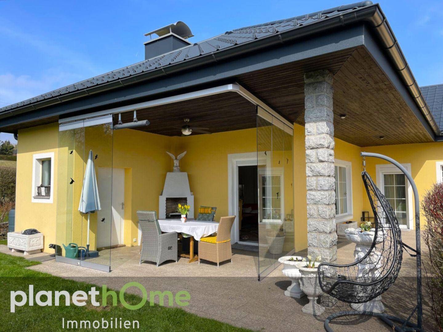 Überdachte Terrasse mit Glaswänden, Gartenmöbeln und Außenkamin für gemütliche Stunden.