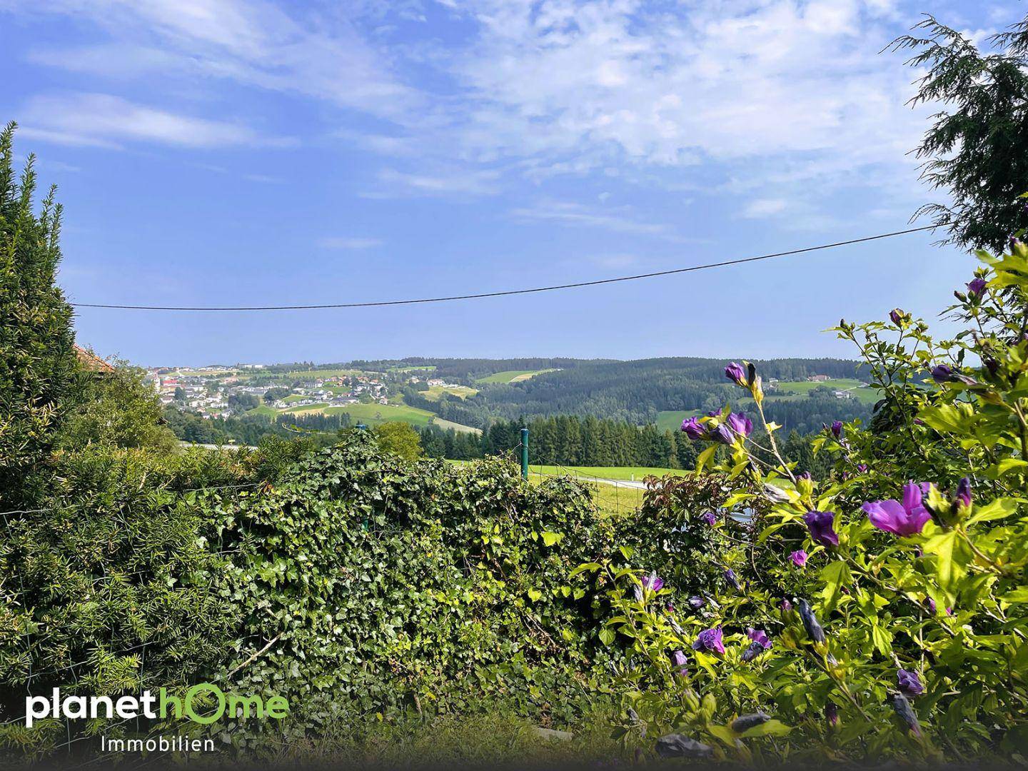 Weitblick über die hügelige Landschaft und eine Ortschaft von der Grundstücksgrenze aus.