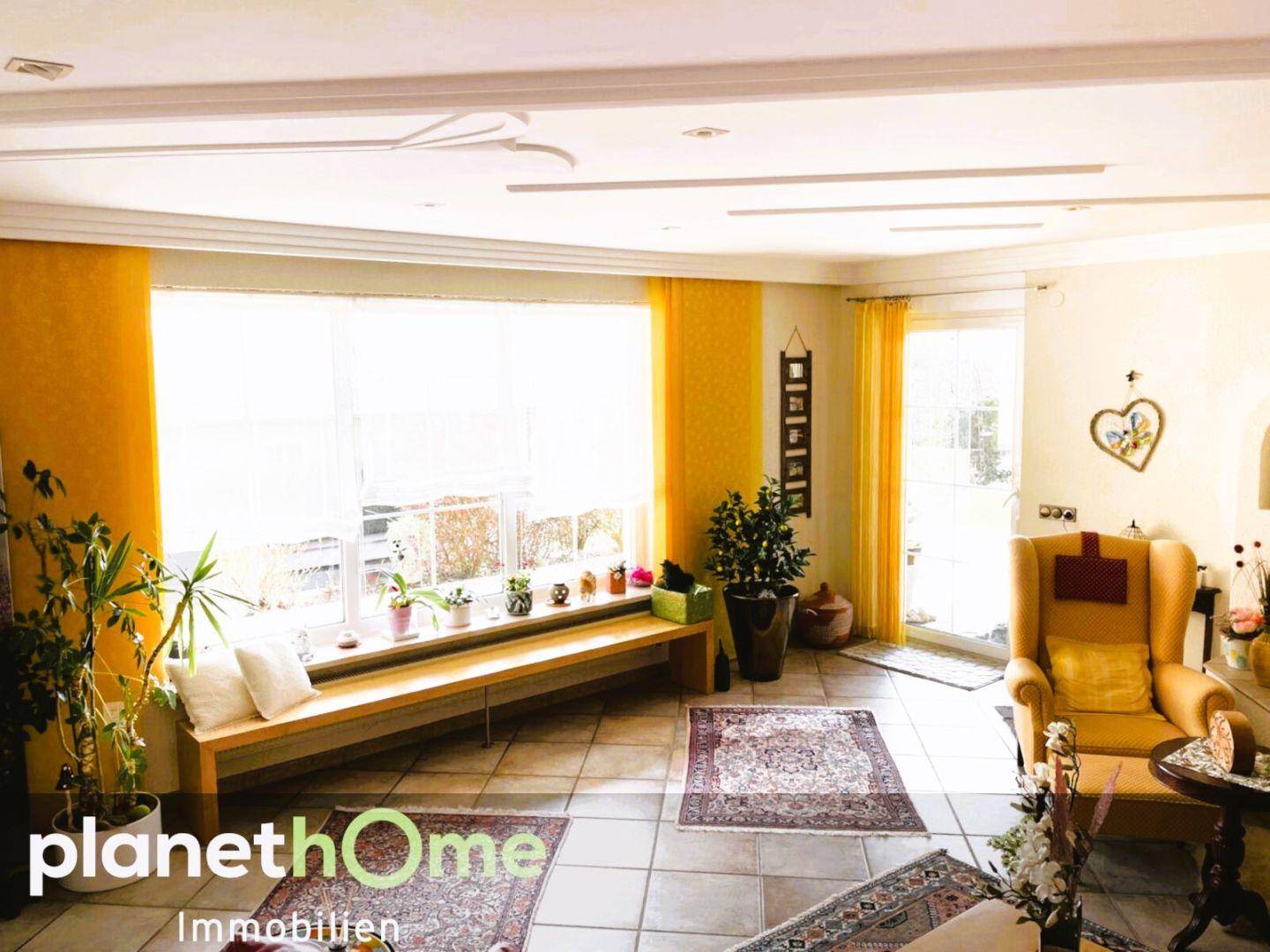 Helles Wohnzimmer mit großen Fenstern, Fliesenboden und Zugang zum Garten.