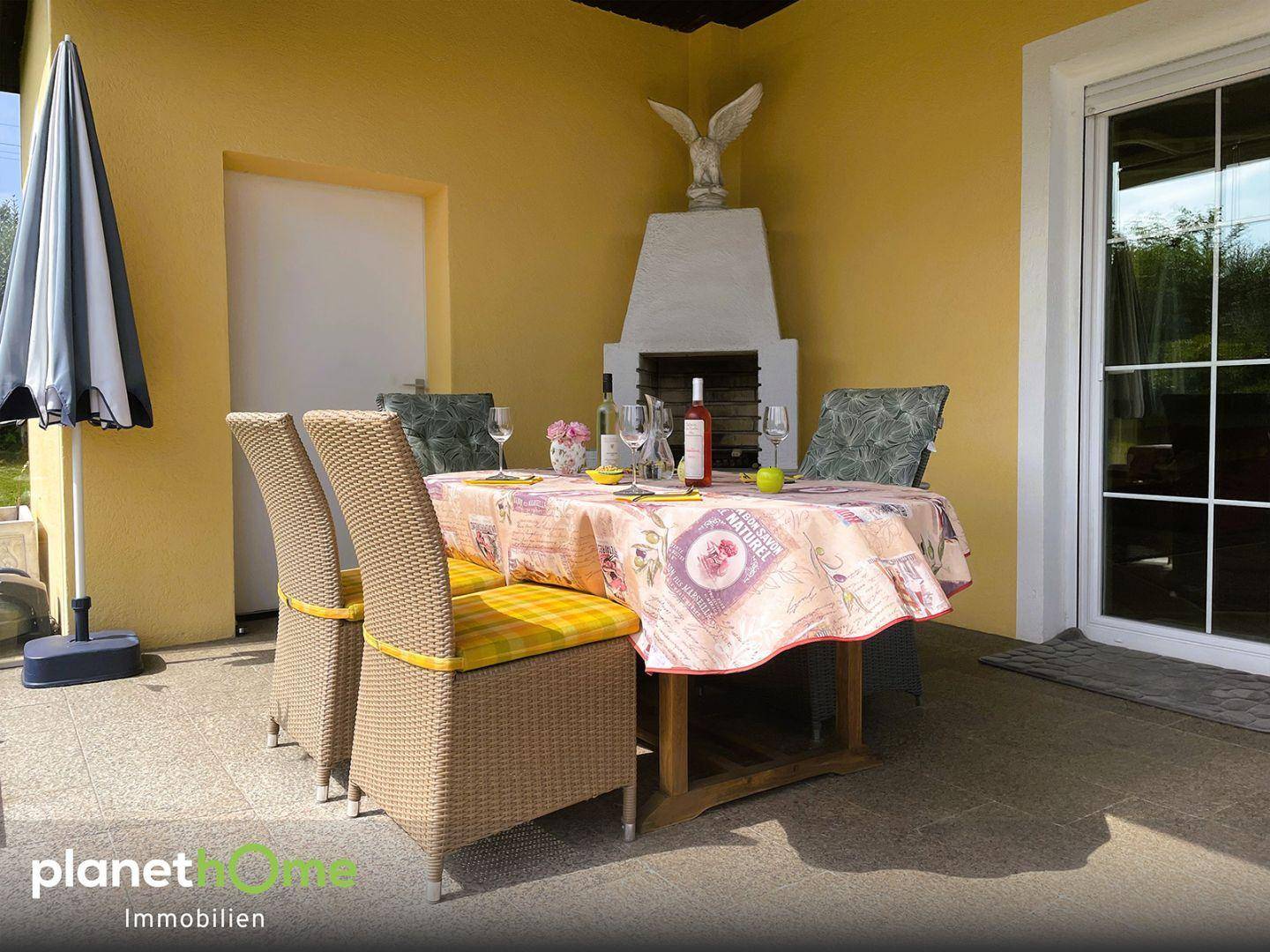 Überdachter Sitzplatz auf der Terrasse mit Esstisch und Außenkamin für Mahlzeiten im Freien.