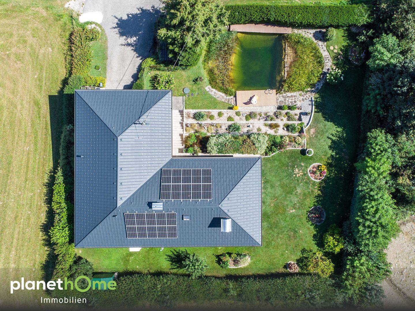 Draufsicht auf das Anwesen mit Haus, Garten, Teich und Photovoltaikanlage auf dem Dach.