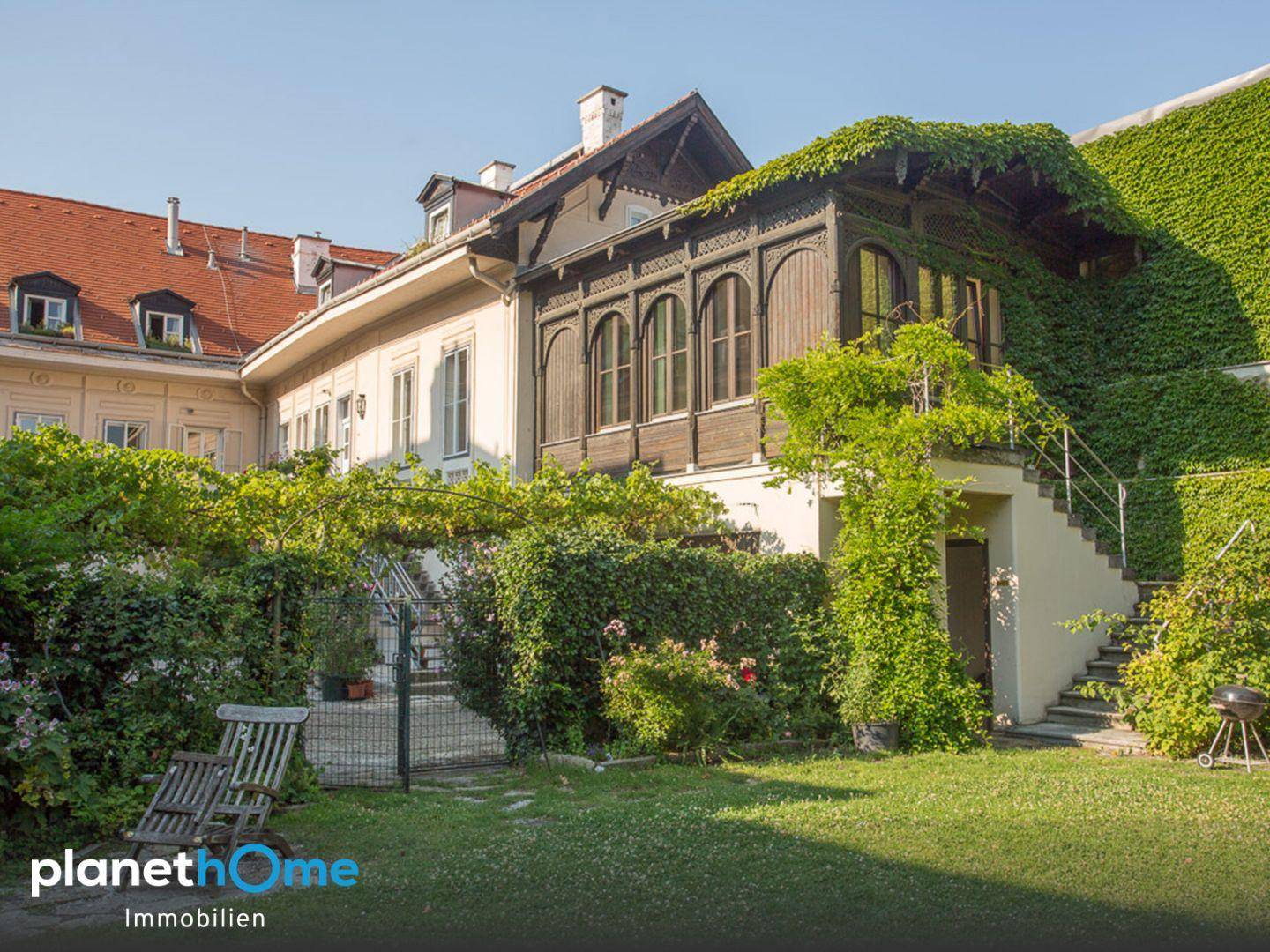 Historische Gebäudefassade mit üppigem Grün, einem gepflegten Garten und Außentreppe.