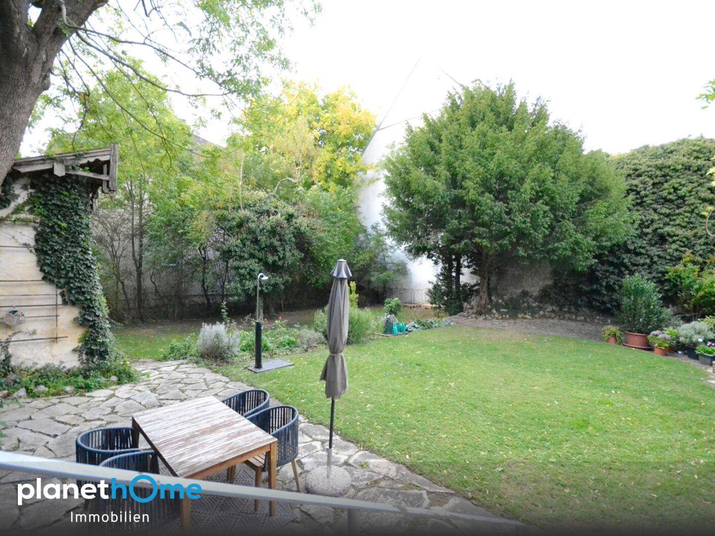 Entspannter Gartenbereich mit Rasenfläche, Bäumen und einer möblierten Terrasse.