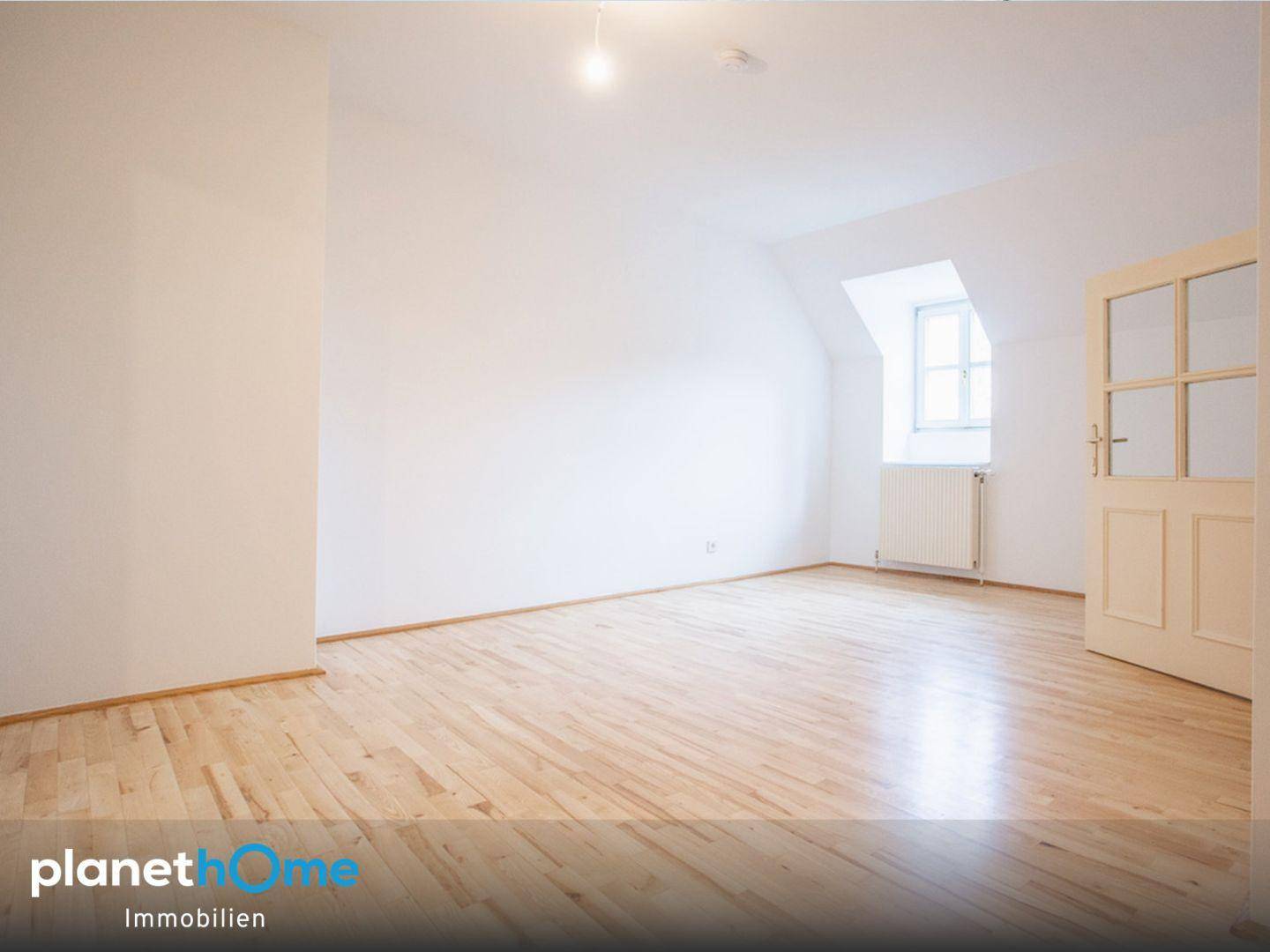 Helles Zimmer mit hellem Holzboden und einem Fenster unter der Dachschräge.