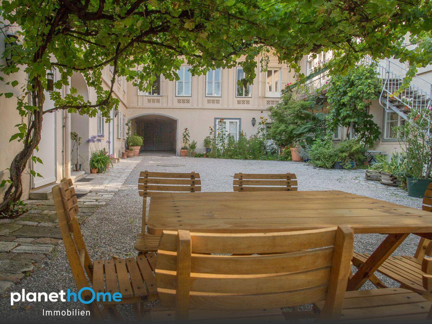 Gemütlicher Essbereich im Freien unter einer bewachsenen Pergola im historischen Innenhof.