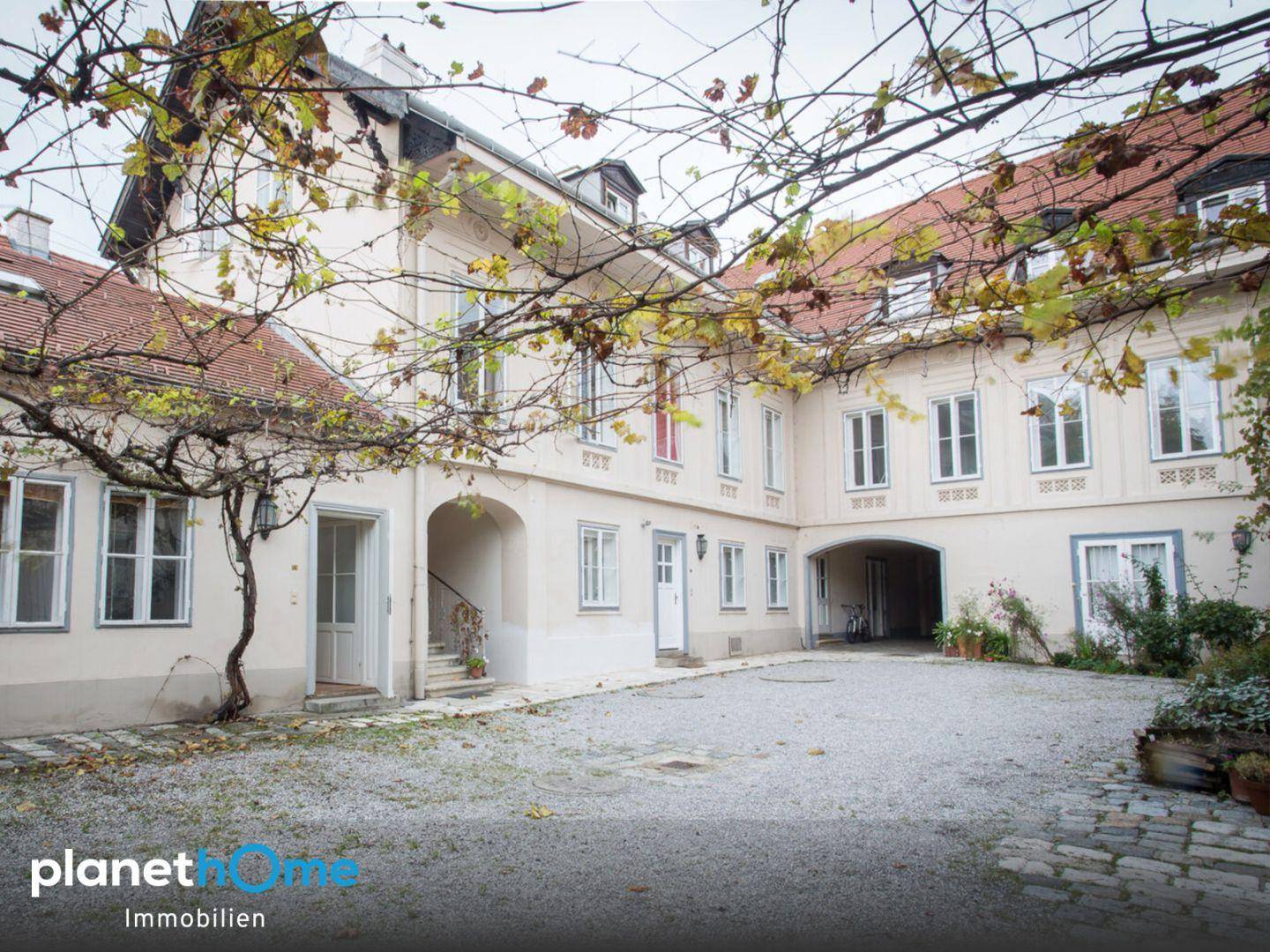 Geräumiger Kieshof umgeben von historischen Gebäuden mit herbstlicher Bepflanzung.