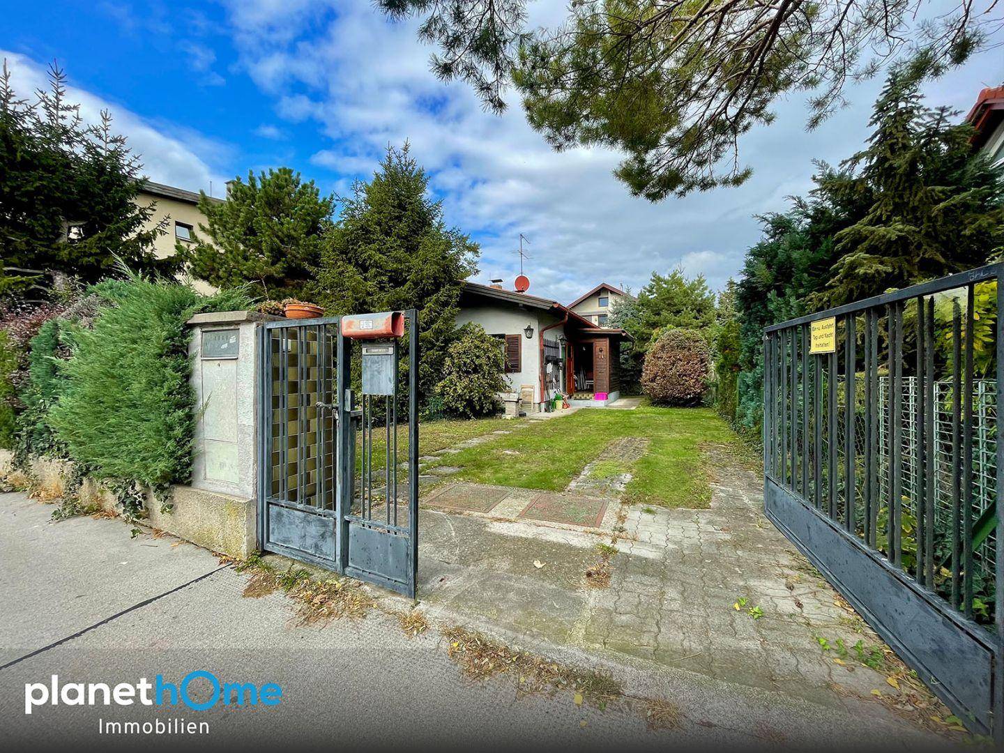 Einfamilienhaus mit offenem Einfahrtstor, großem Vorgarten und Zufahrt zum Grundstück.