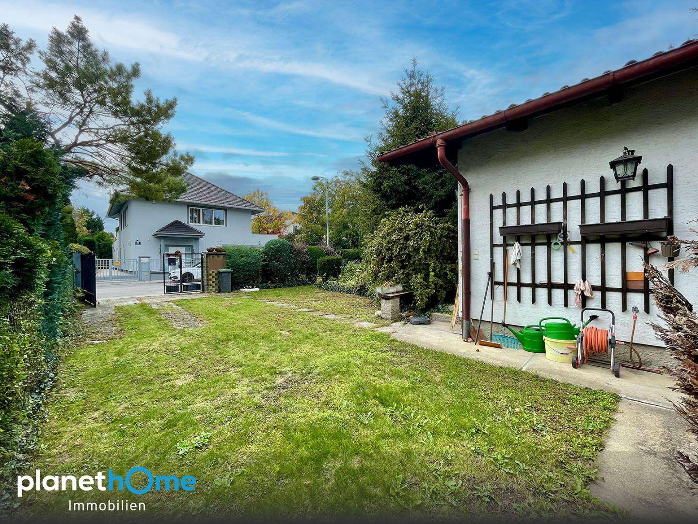 Rückseite des Hauses mit Garten, Rasenfläche und Gartengeräten an der Hauswand.