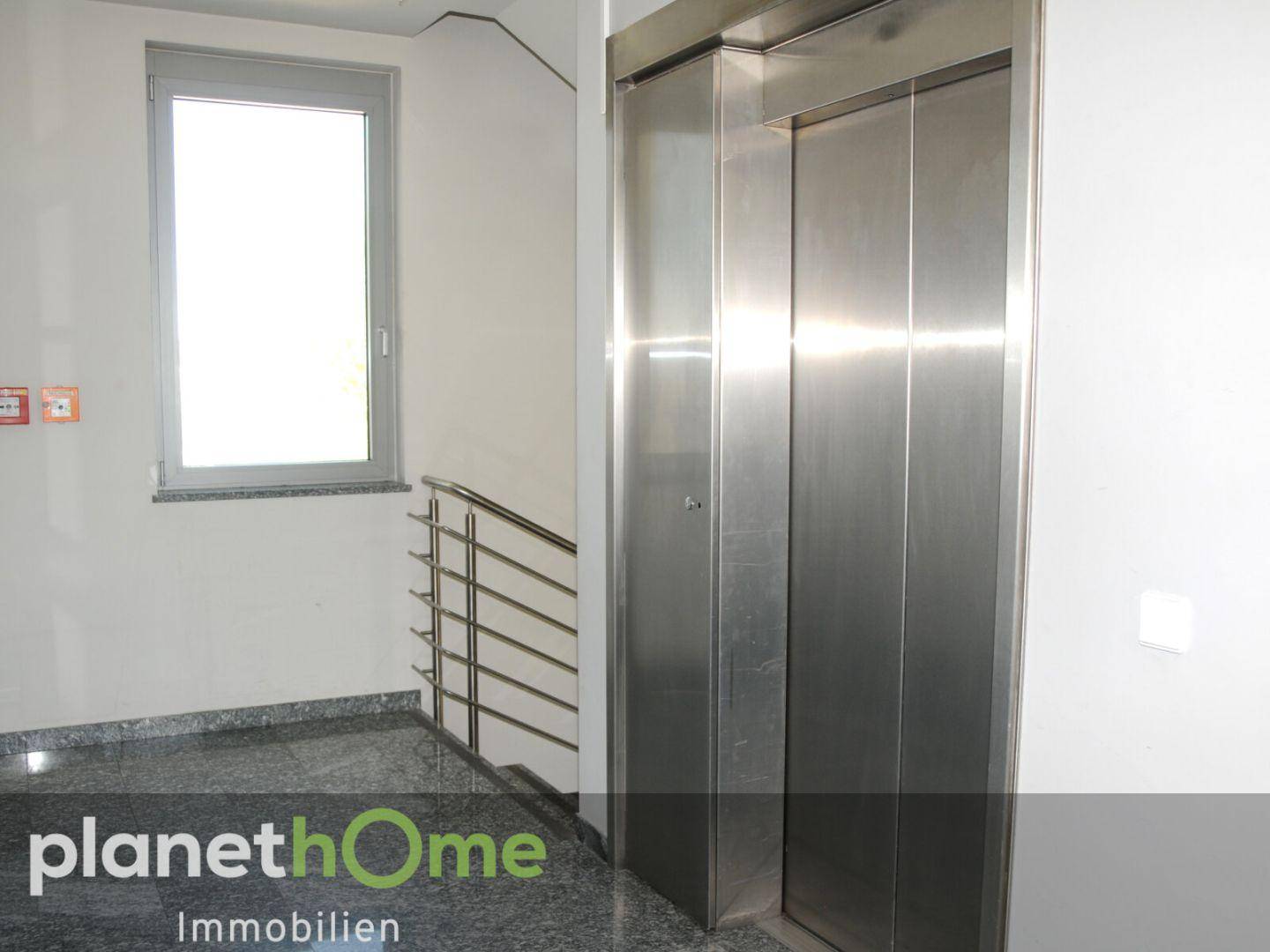 Moderner Aufzug und Treppenabsatz mit Granitboden und Fenster, bietet Zugang zu allen Stockwerken.
