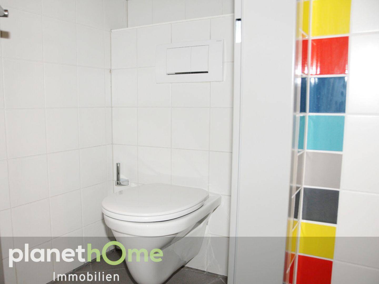 Wandhängendes WC in einem hell gefliesten Raum mit farbigen Akzenten.