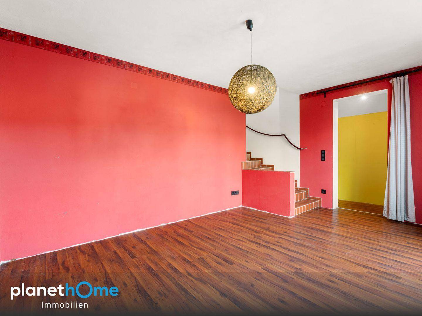 Heller Raum mit roten Wänden, Holzboden und einer Treppe, die in eine andere Etage führt.