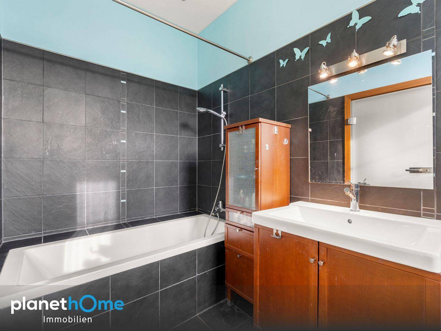 Badezimmer mit Badewanne, Einzelwaschbecken und dunklen Fliesen, dekoriert mit Schmetterlingen.