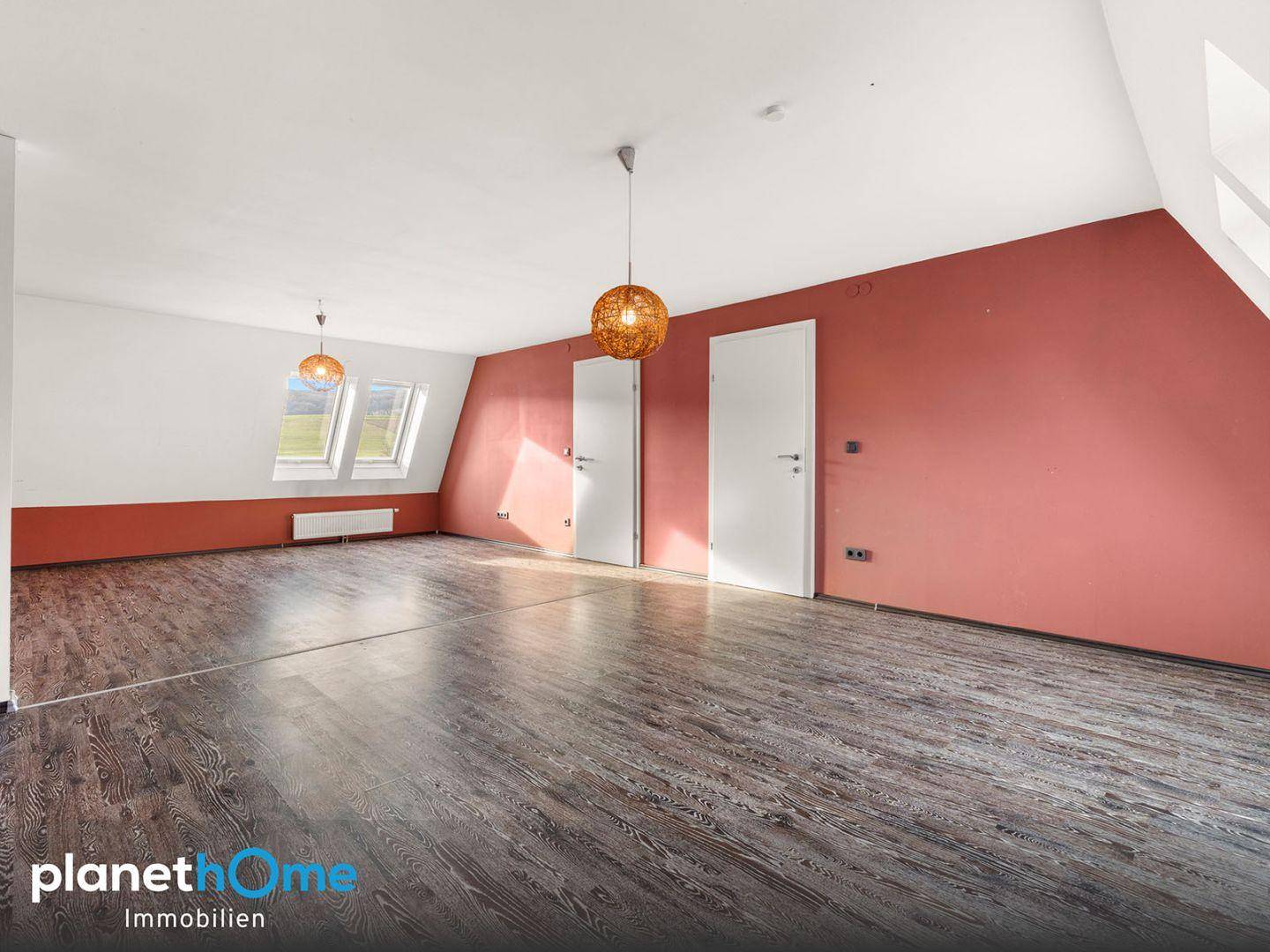 Helles Dachgeschosszimmer mit schrägen Wänden, Dachfenstern und Holzboden.