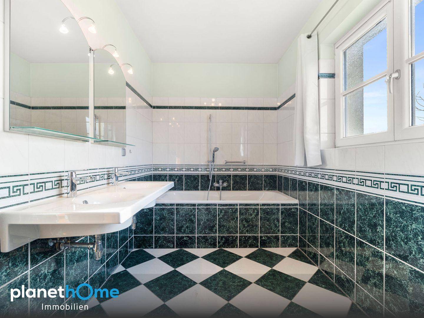 Badezimmer mit Badewanne, Einzelwaschbecken und auffälligen grün-weißen Fliesen.