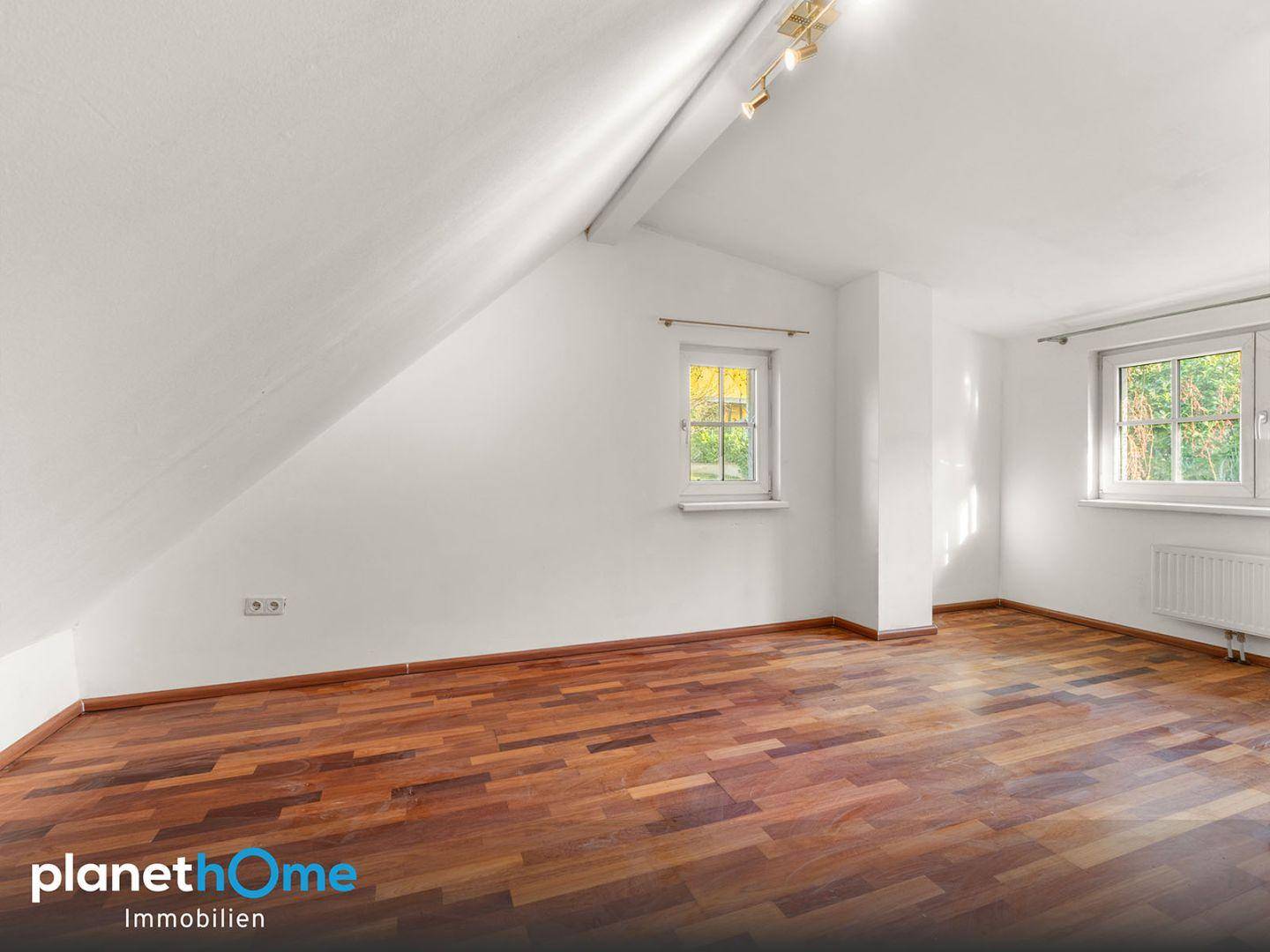 Geräumiges Dachgeschosszimmer mit schrägen Wänden, Holzboden und zwei Fenstern.