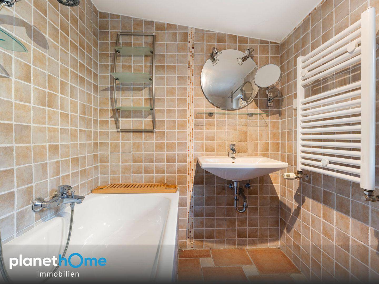 Badezimmer mit Badewanne, Einzelwaschbecken und beigefarbenen Fliesen, inklusive Handtuchheizkörper.