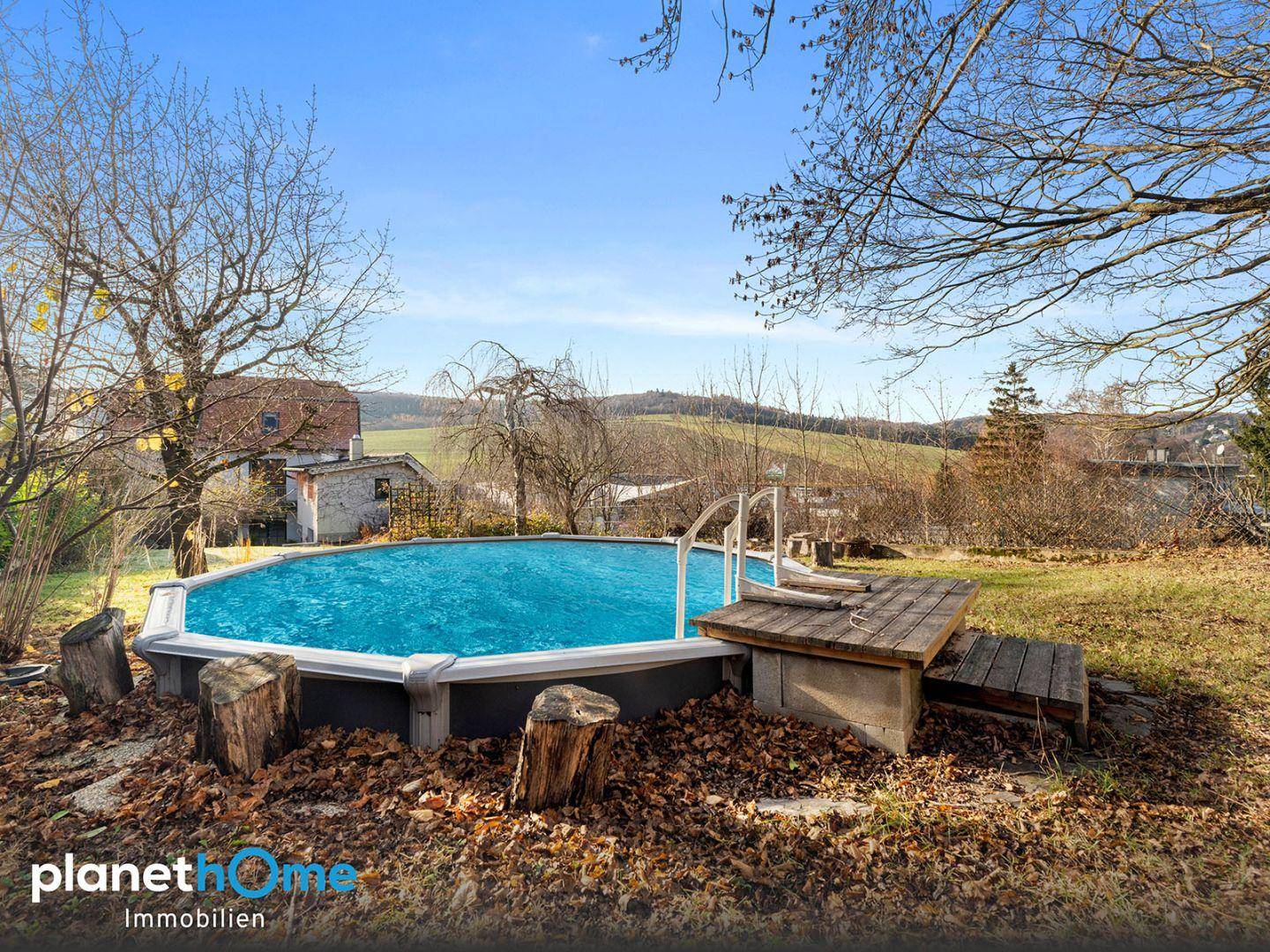 Gartenbereich mit einem Aufstellpool und Holzdeck, umgeben von Bäumen und Natur.