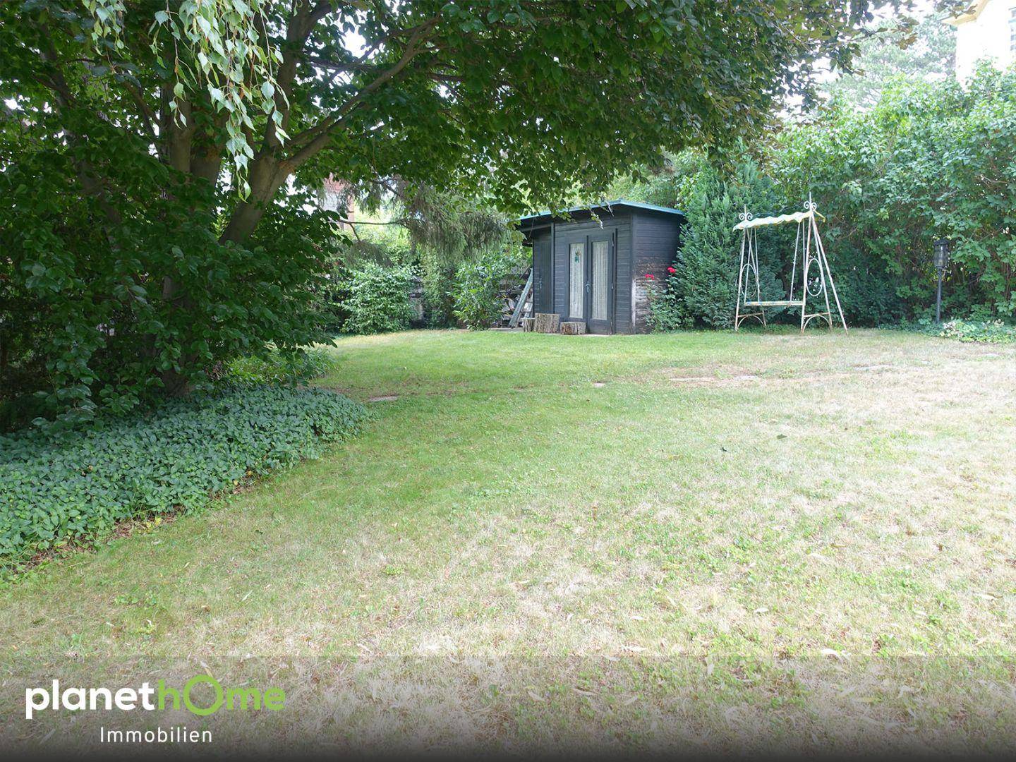 Gepflegter Garten mit Rasenfläche, einem kleinen Gartenhaus und einer Schaukel unter einem großen Baum.