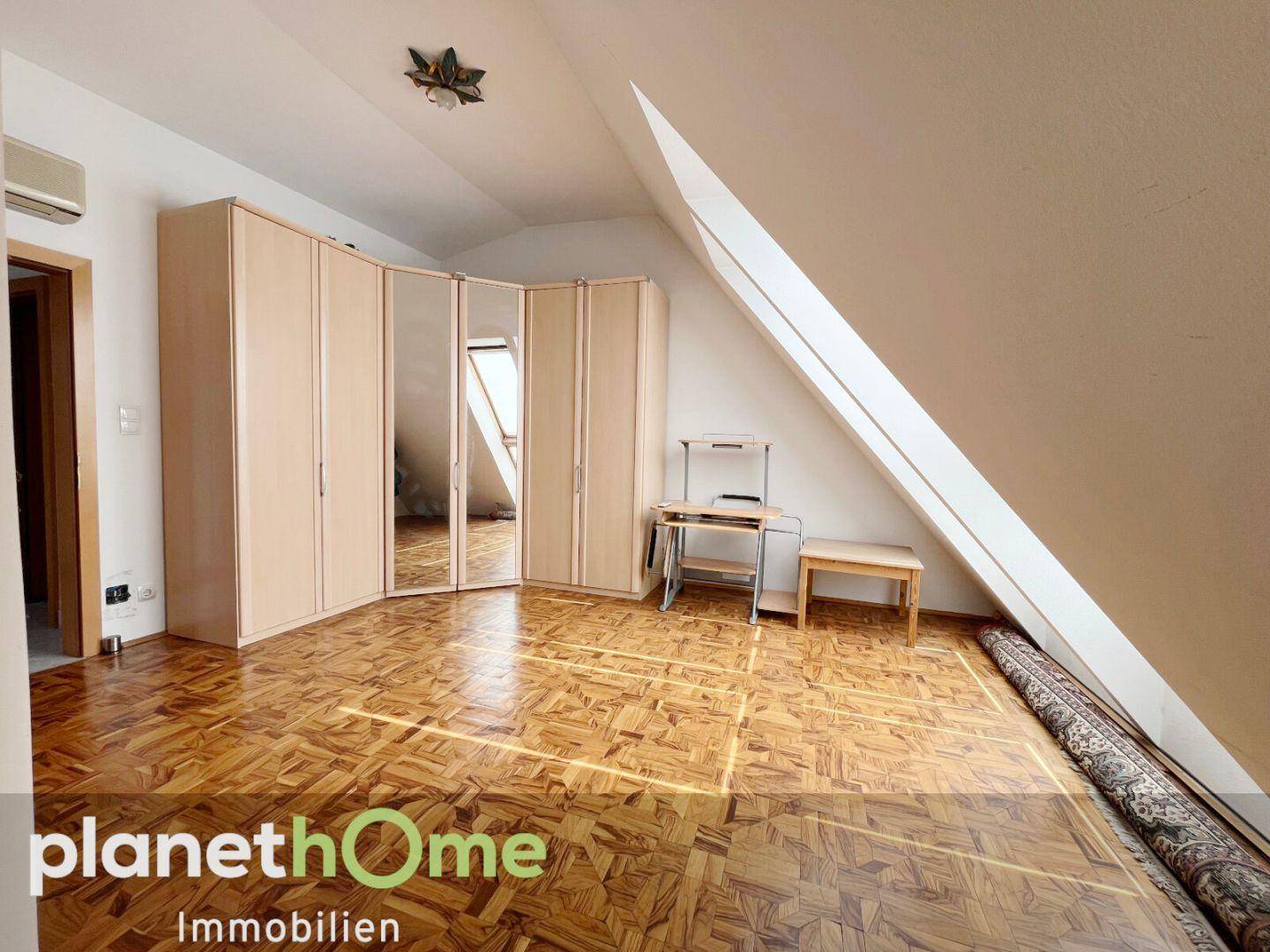 Geräumiges Dachgeschosszimmer mit Parkettboden, Schrägdach und Eckkleiderschrank.