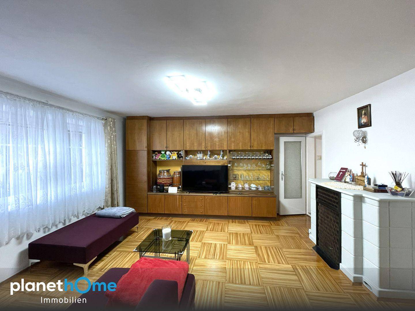 Gemütliches Wohnzimmer mit Parkettboden, großem Wandschrank und einem traditionellen Kaminofen.