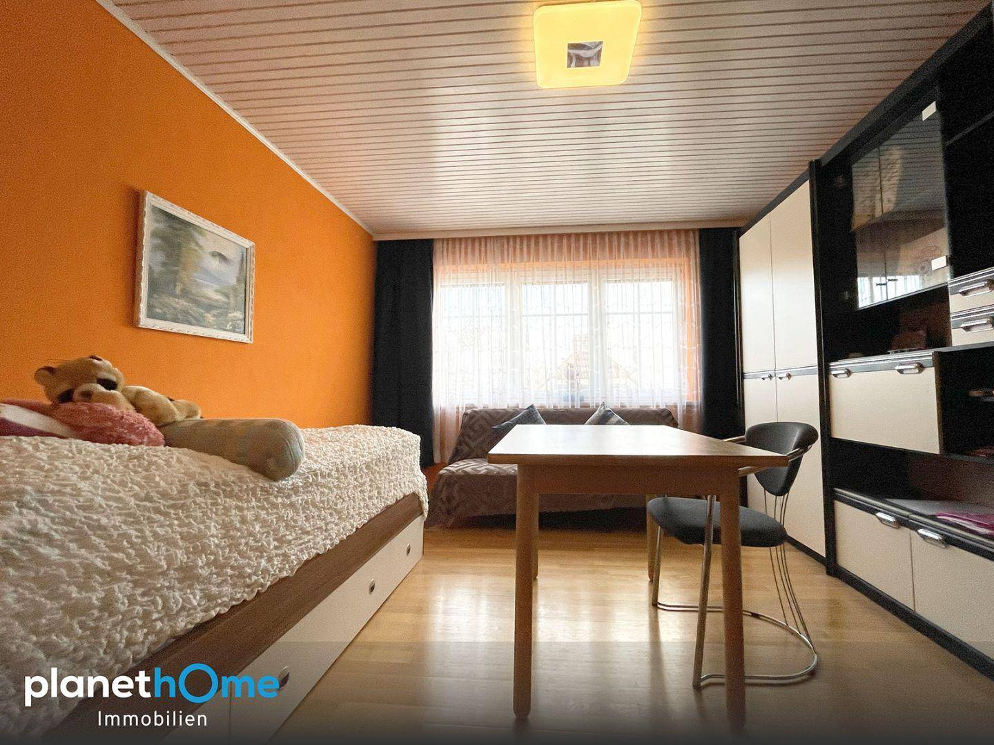 Farbiges Schlafzimmer mit orangefarbener Wand, Holzfußboden und großem Fenster.