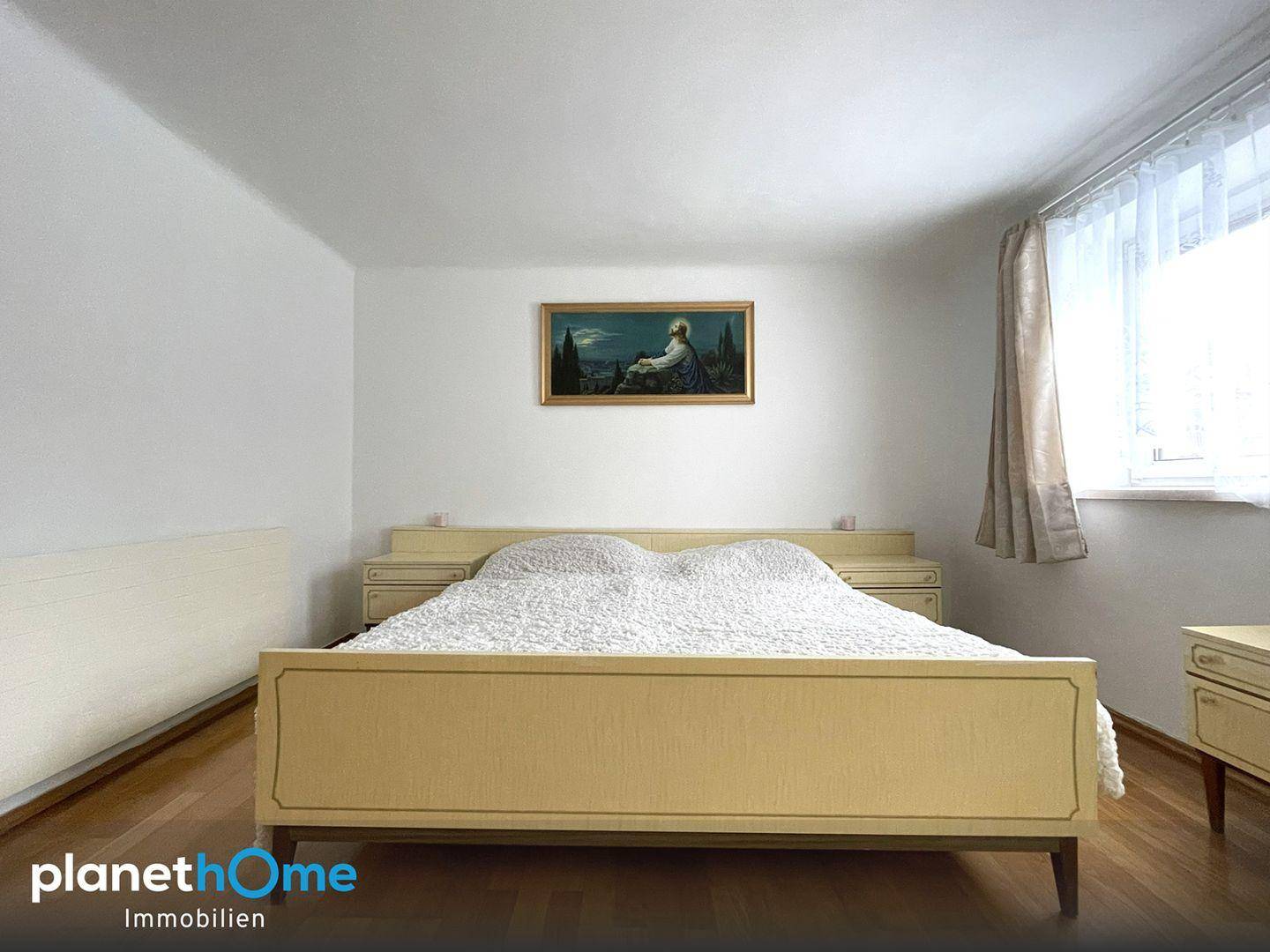 Helles Schlafzimmer mit Doppelbett, Holzparkett und einem Fenster für natürliches Licht.