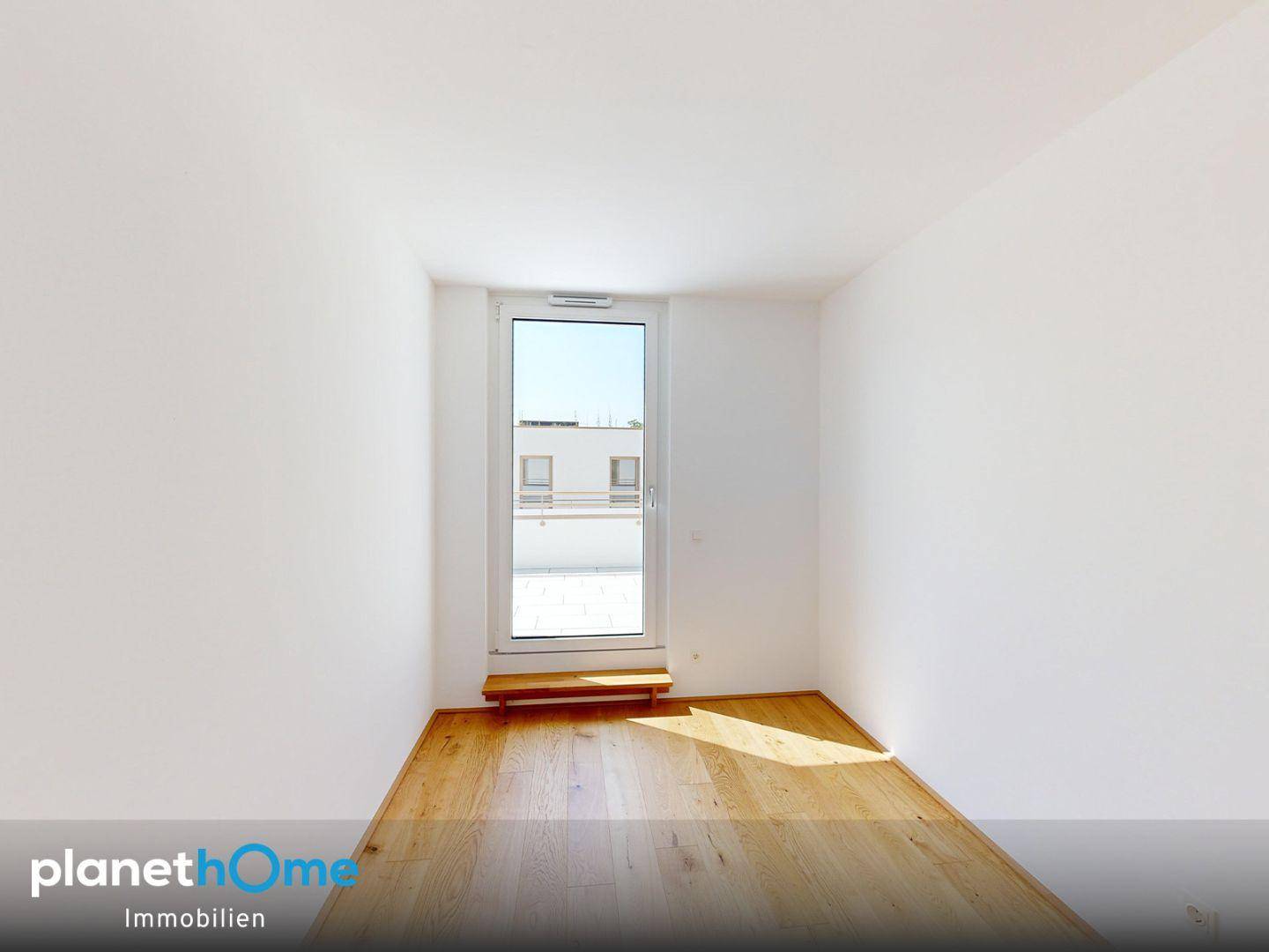 Freundliches, leeres Zimmer mit Holzboden und Zugang zu einem Außenbereich.