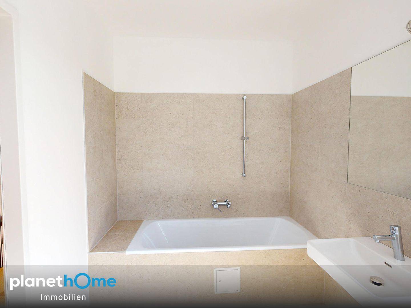 Modernes Badezimmer mit Badewanne, beigefarbenen Fliesen und weißem Waschbecken.