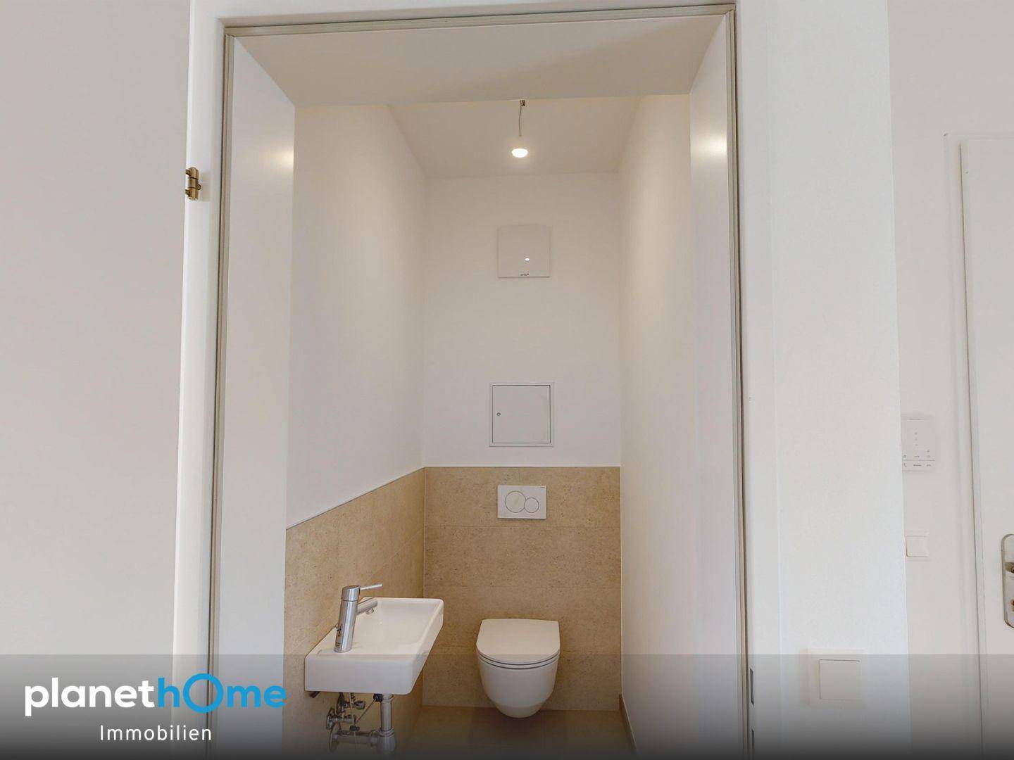 Separates Gäste-WC mit Wand-WC, kleinem Waschbecken und beigefarbenen Fliesen.