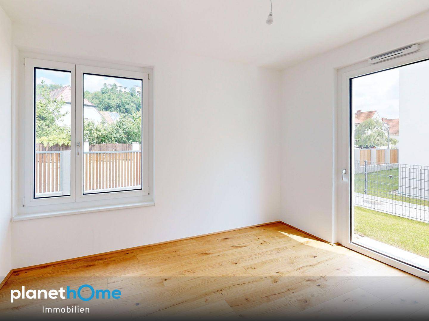 Helles Schlafzimmer mit Holzboden und Fenster mit Blick auf den Gartenbereich.