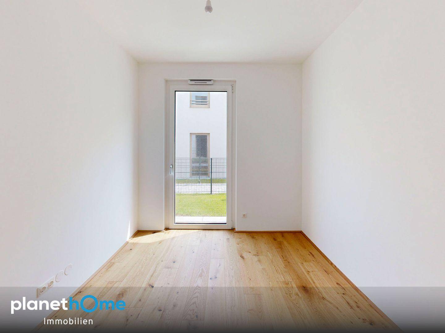 Leeres Zimmer mit Holzboden und einer Tür, die ins Freie führt, ideal als Schlafzimmer.