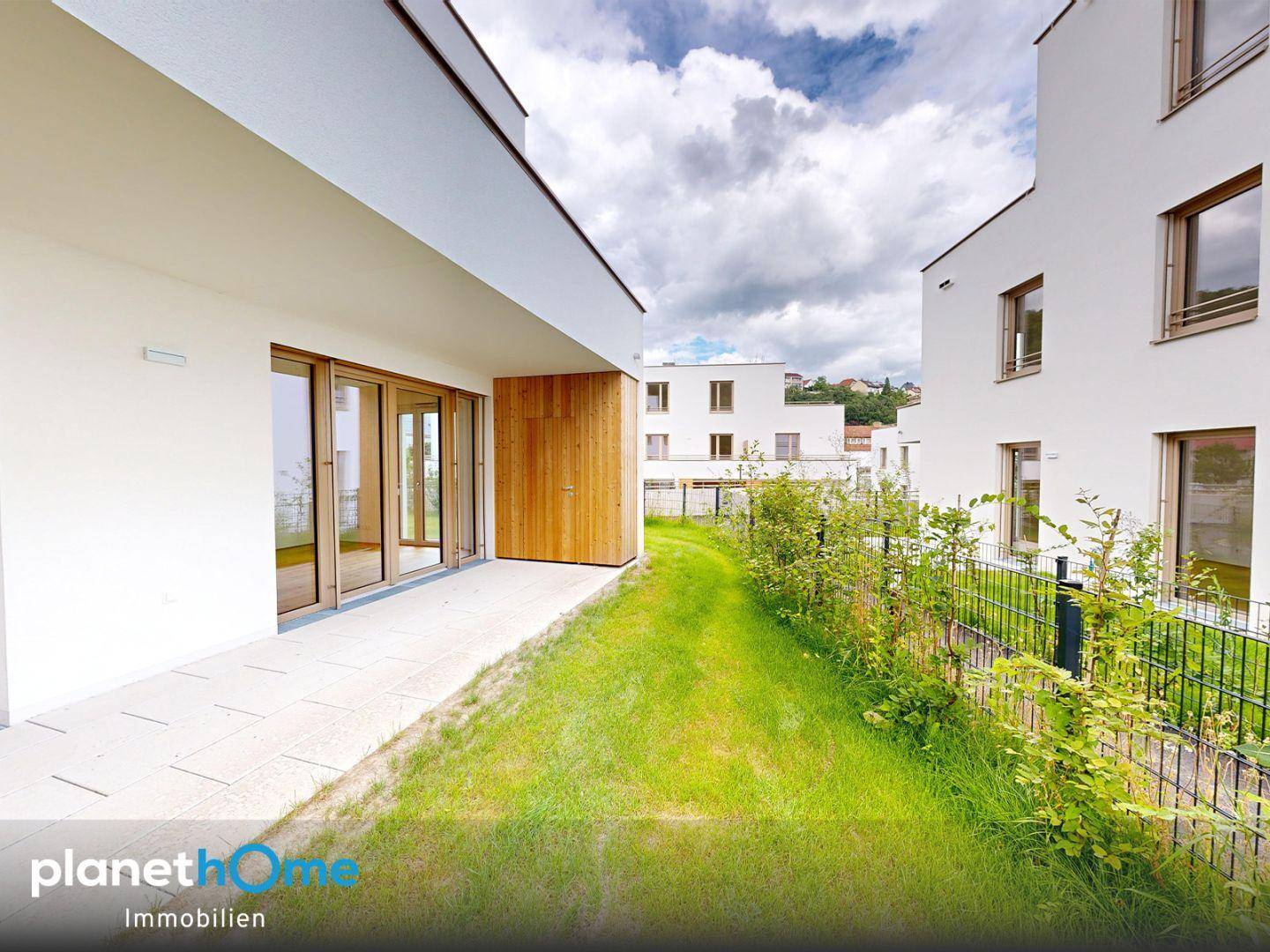 Gepflegter Gartenbereich mit Rasenfläche und Terrasse, umgeben von modernen Wohngebäuden.