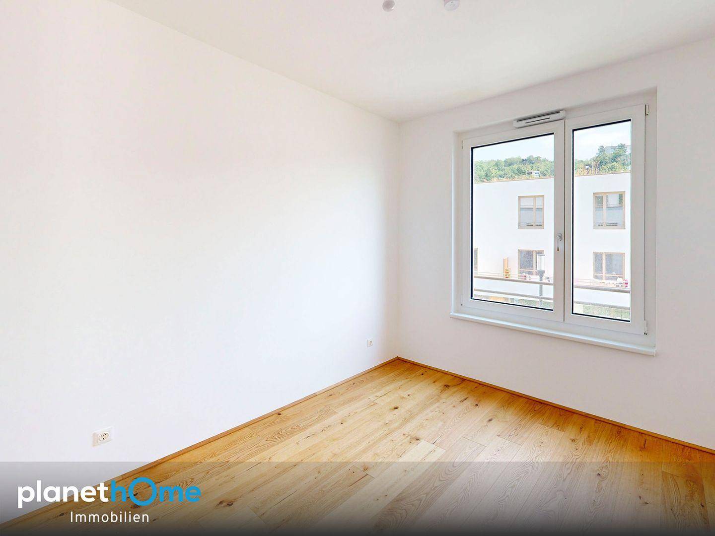 Helles Schlafzimmer mit Holzboden und Blick auf die benachbarten Gebäude.