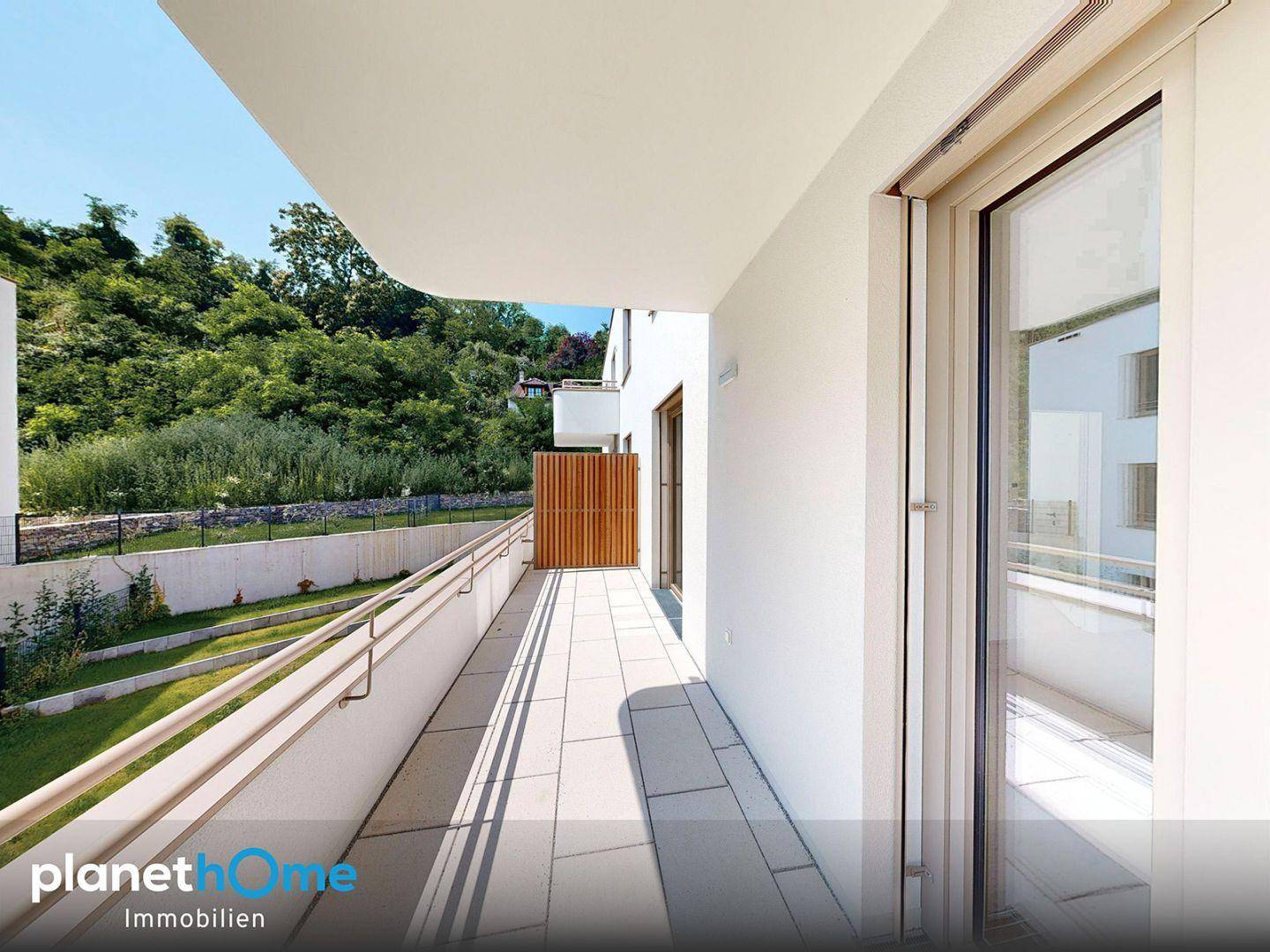 Langer, moderner Balkon mit Fliesenboden und Blick auf eine grüne Hügellandschaft.
