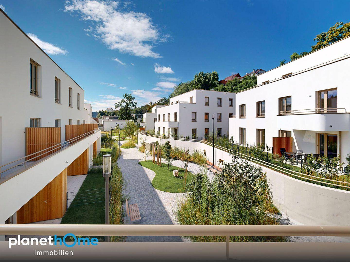Luftaufnahme einer modernen Wohnsiedlung in einer grünen Hügellandschaft mit Stadtblick.