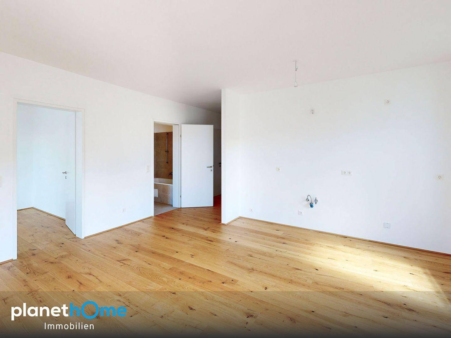 Helles Zimmer mit Parkettboden und großem Fenster, das Zugang zu einem Balkon bietet.