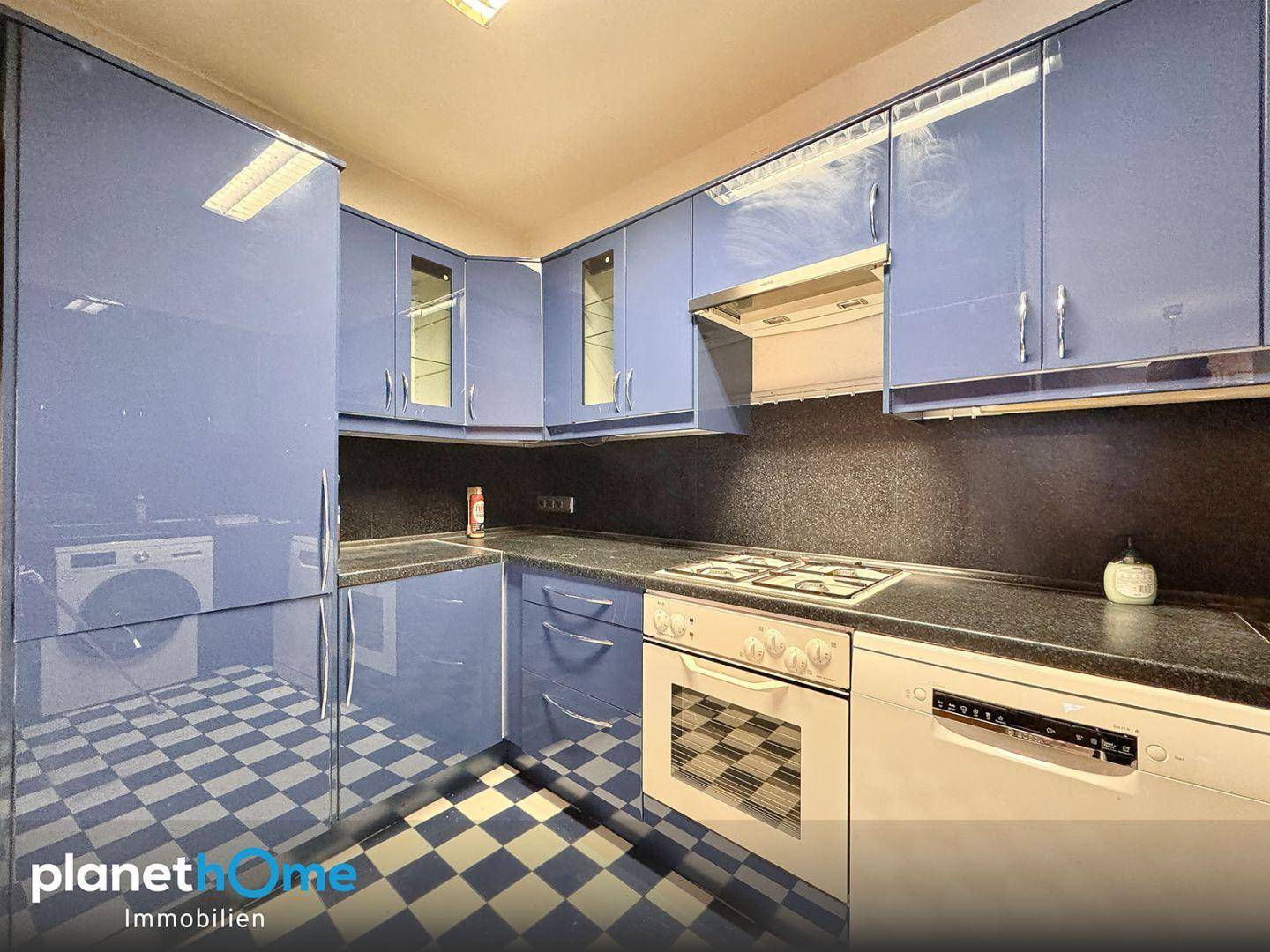 Blaue Küche mit glänzenden Fronten, Gasherd, Backofen und Schachbrettmuster-Fliesenboden.