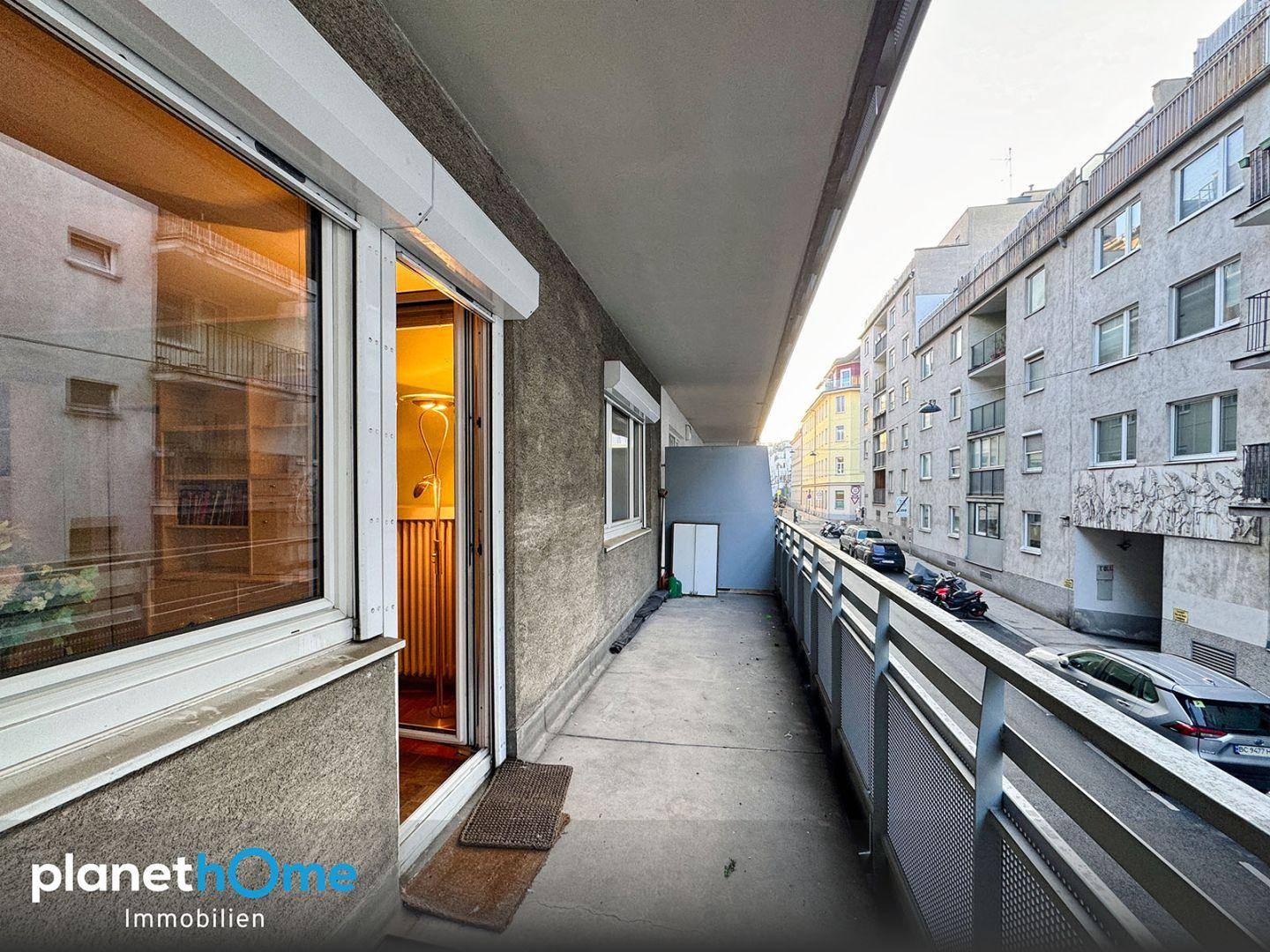 Langer Balkon mit Blick auf die Straße und die angrenzenden Gebäude, ausgestattet mit Rollläden.
