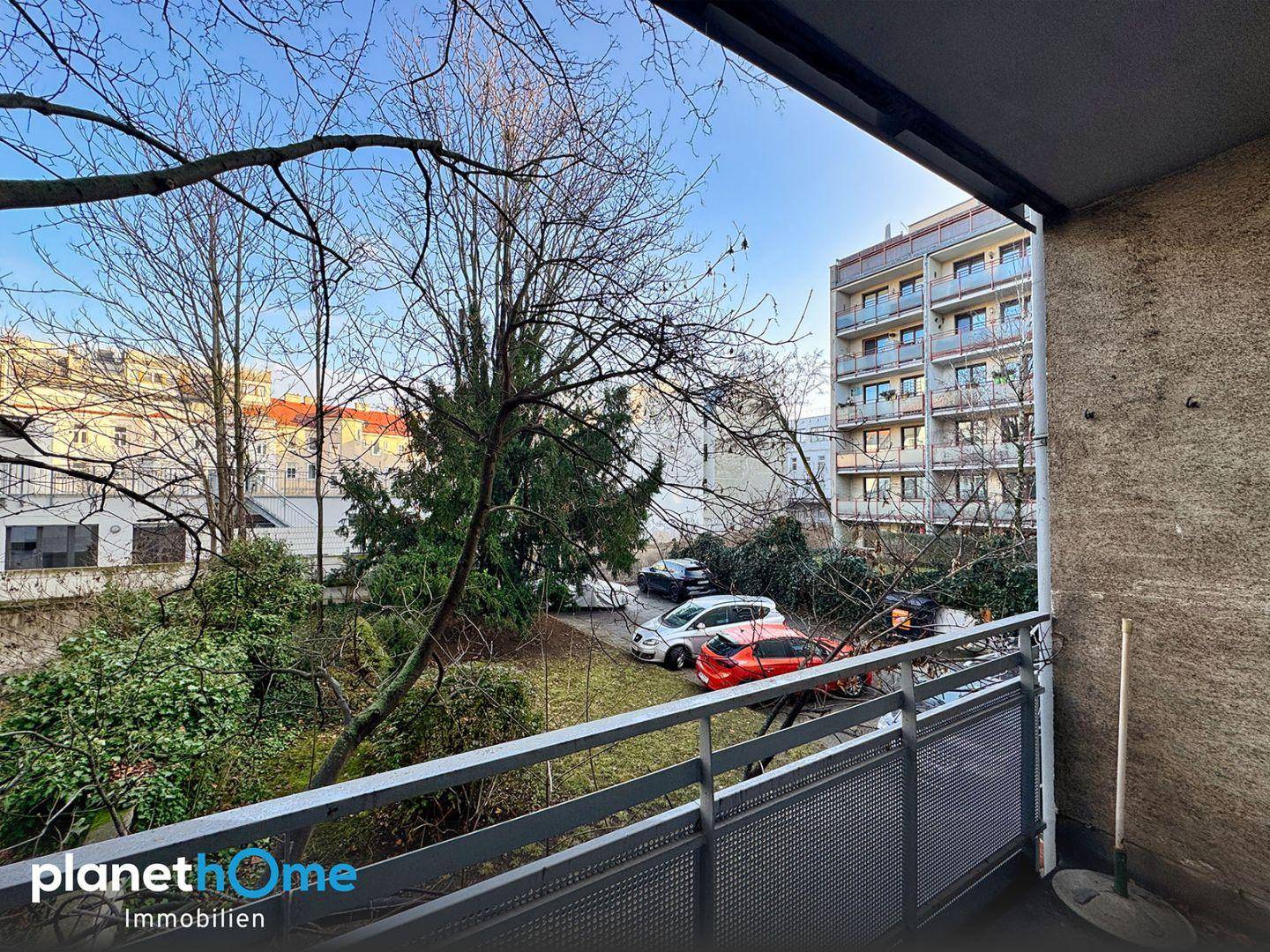 Balkon mit Blick auf einen begrünten Innenhof und umliegende Gebäude an einem sonnigen Tag.