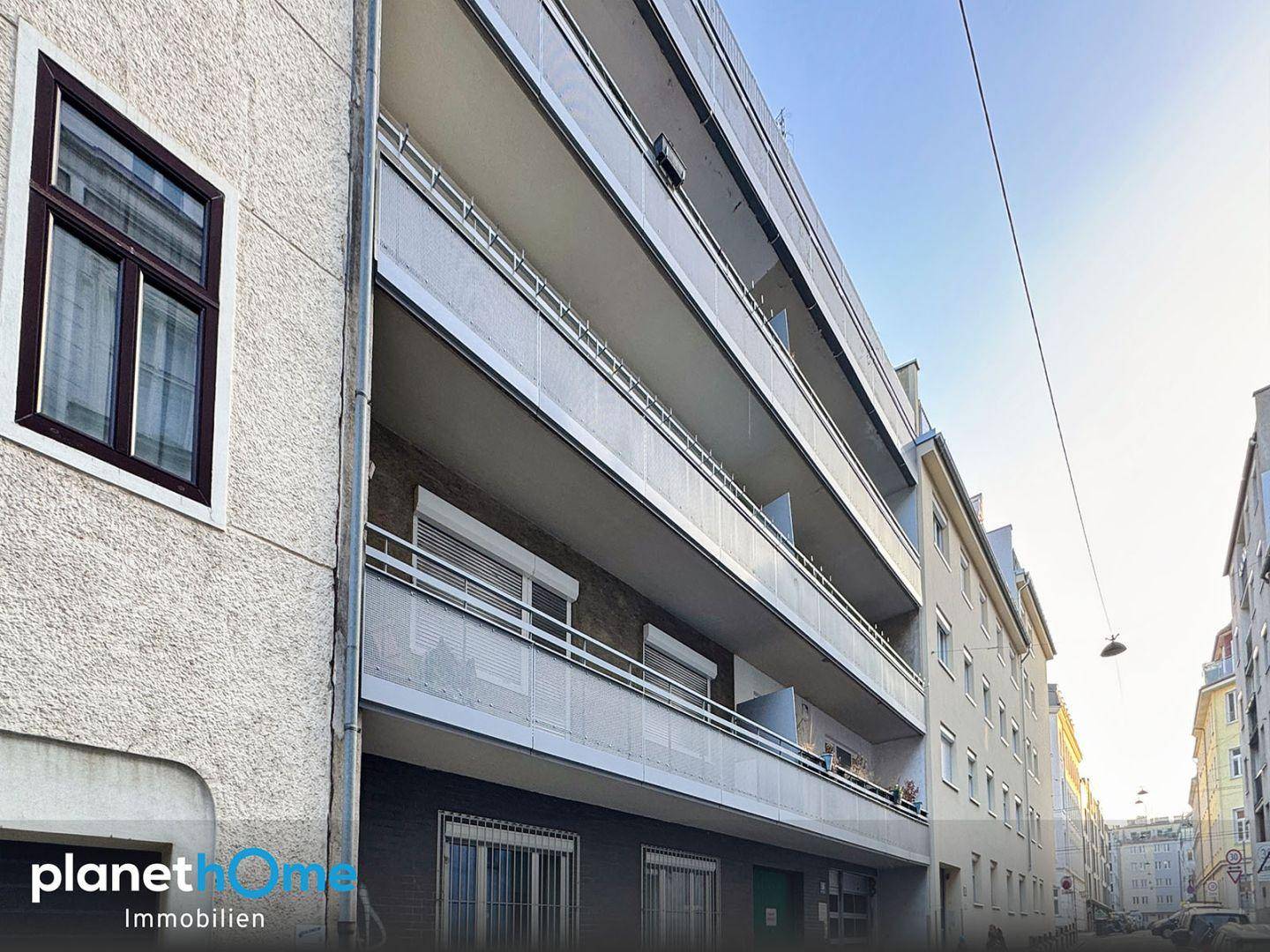 Fassade eines Wohngebäudes mit mehreren Balkonen und Fenstern entlang einer Stadtstraße.