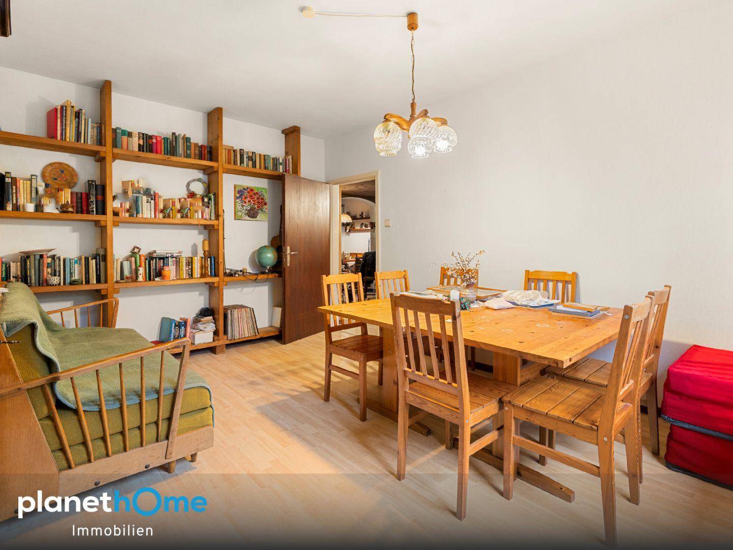 Gemütlicher Essbereich mit großem Holztisch, Stühlen und einem Bücherregal an der Wand.