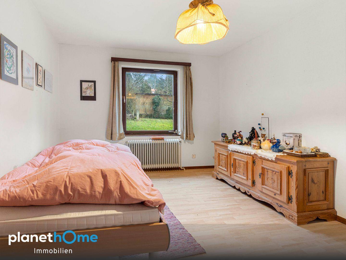 Schlafzimmer mit Einzelbett, rustikaler Holzkommode und Blick in den grünen Garten.