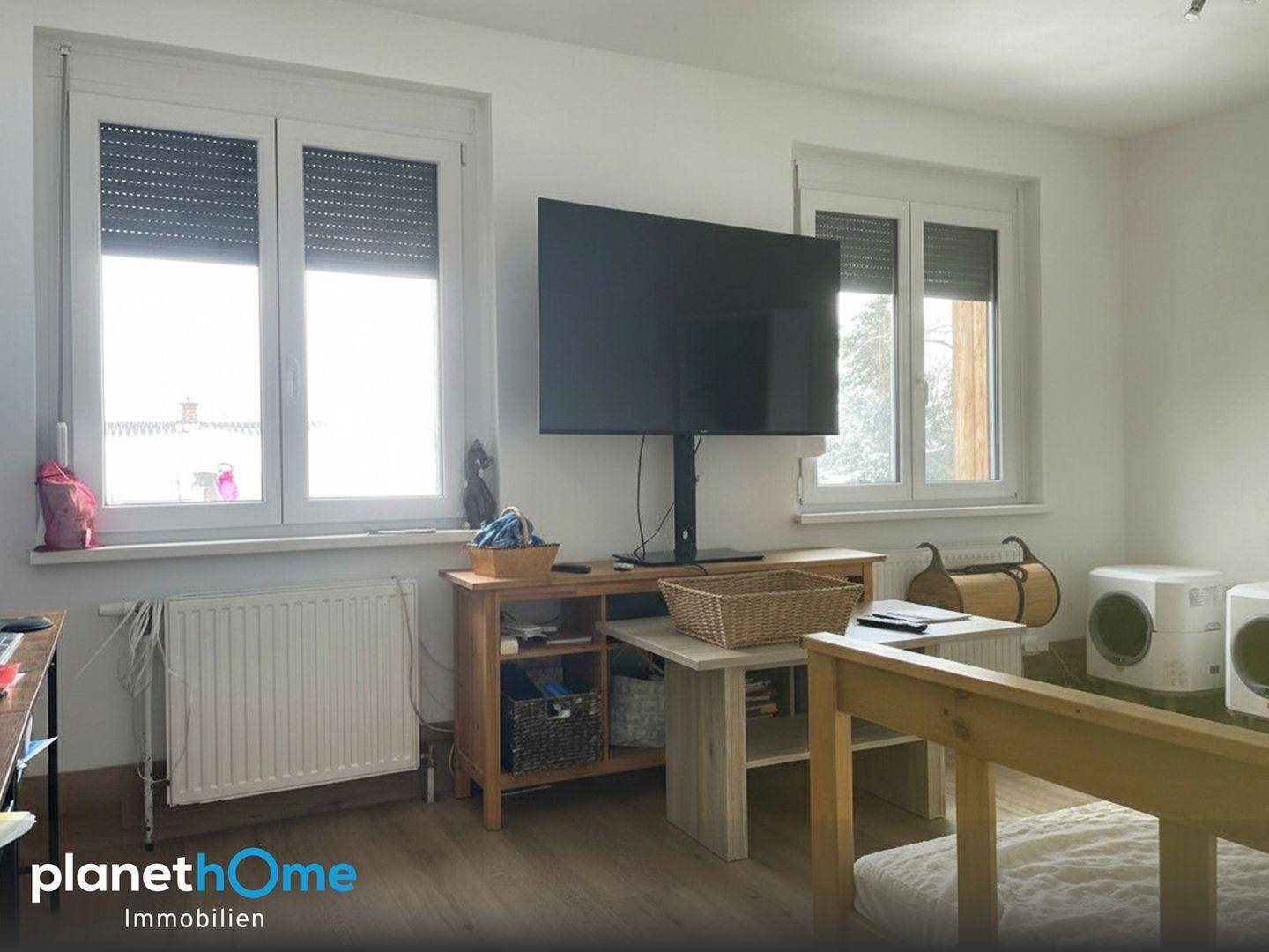 Helles Zimmer mit zwei Fenstern, Rollläden und einem Fernseher.