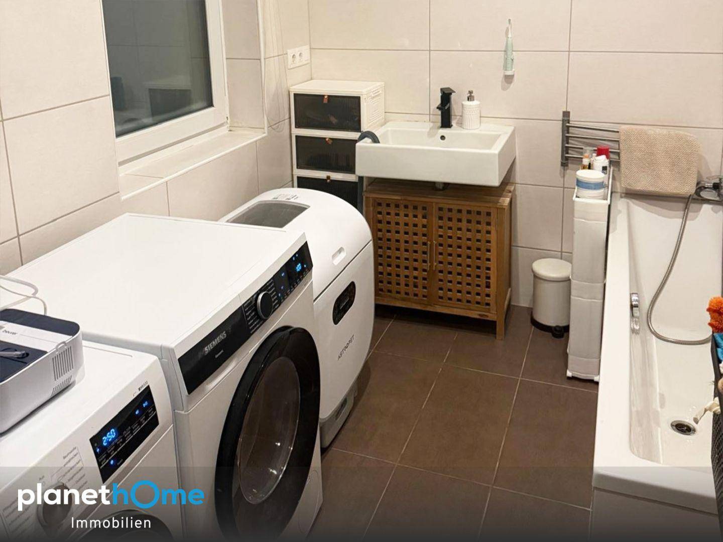 Badezimmer mit Badewanne, Waschbecken, Waschmaschine und hellen Fliesen.