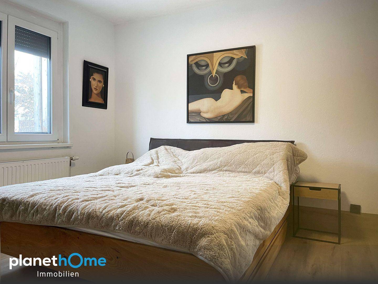 Schlafzimmer mit großem Bett, Fenster und moderner Kunst an den Wänden.