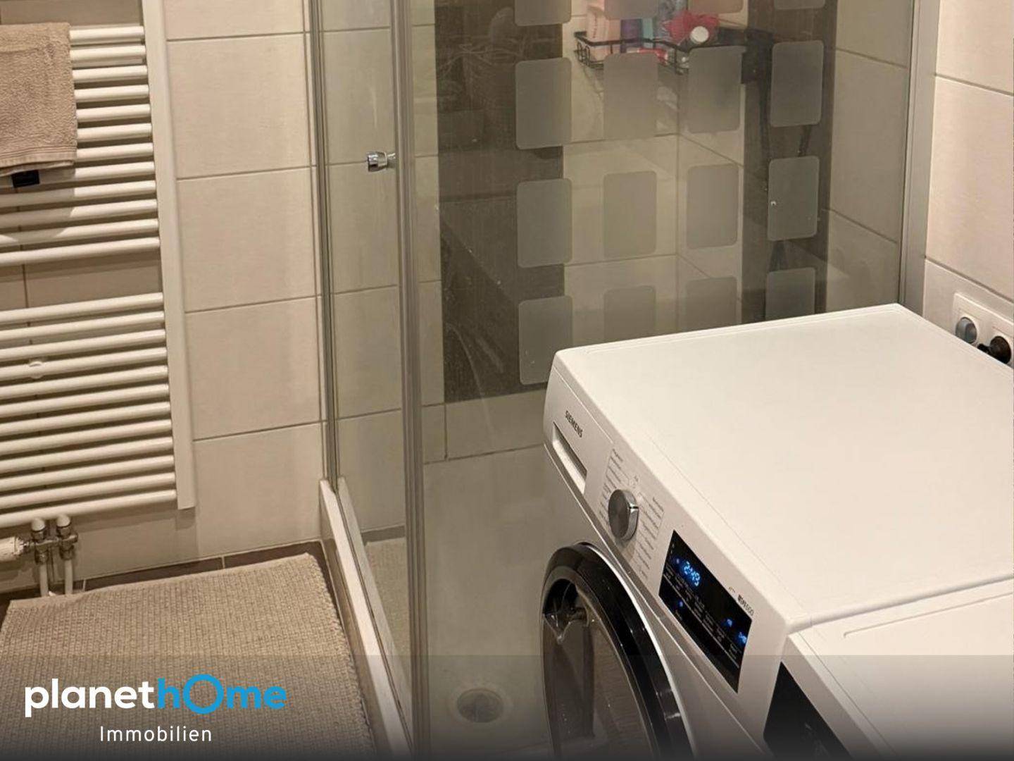 Duschbereich mit Glasabtrennung und Waschmaschine im Badezimmer.
