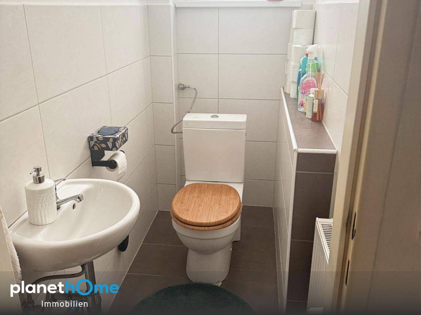 Kleines Gäste-WC mit Toilette, Waschbecken und hellen Fliesen.