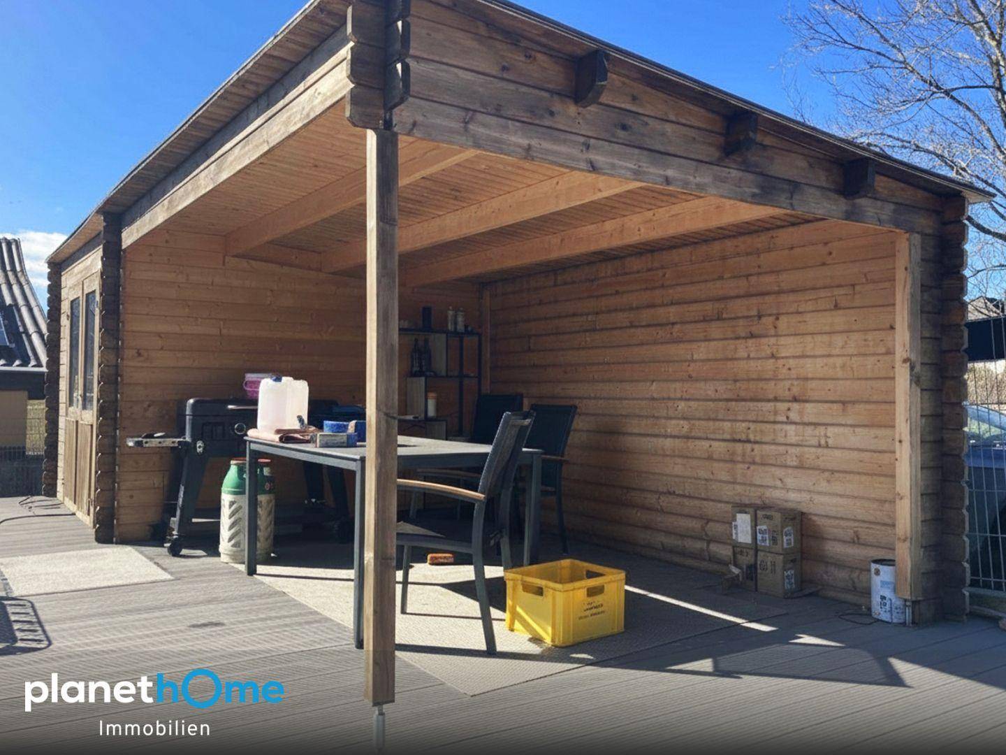 Überdachte Holzterrasse mit Grillbereich und Sitzgelegenheiten im Freien.